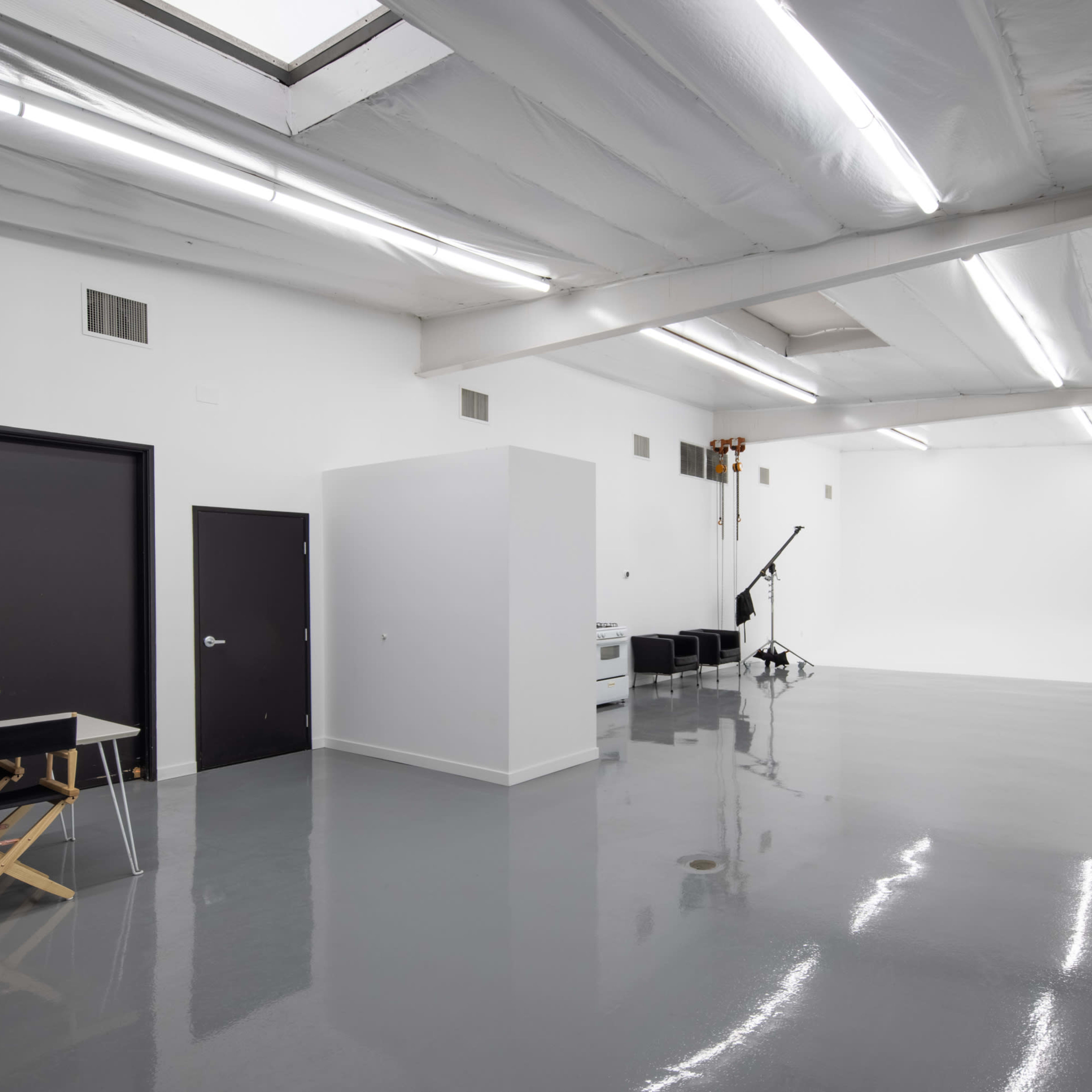A spacious, brightly lit studio with polished concrete flooring, featuring black doors, a white partition, and a backdrop area.