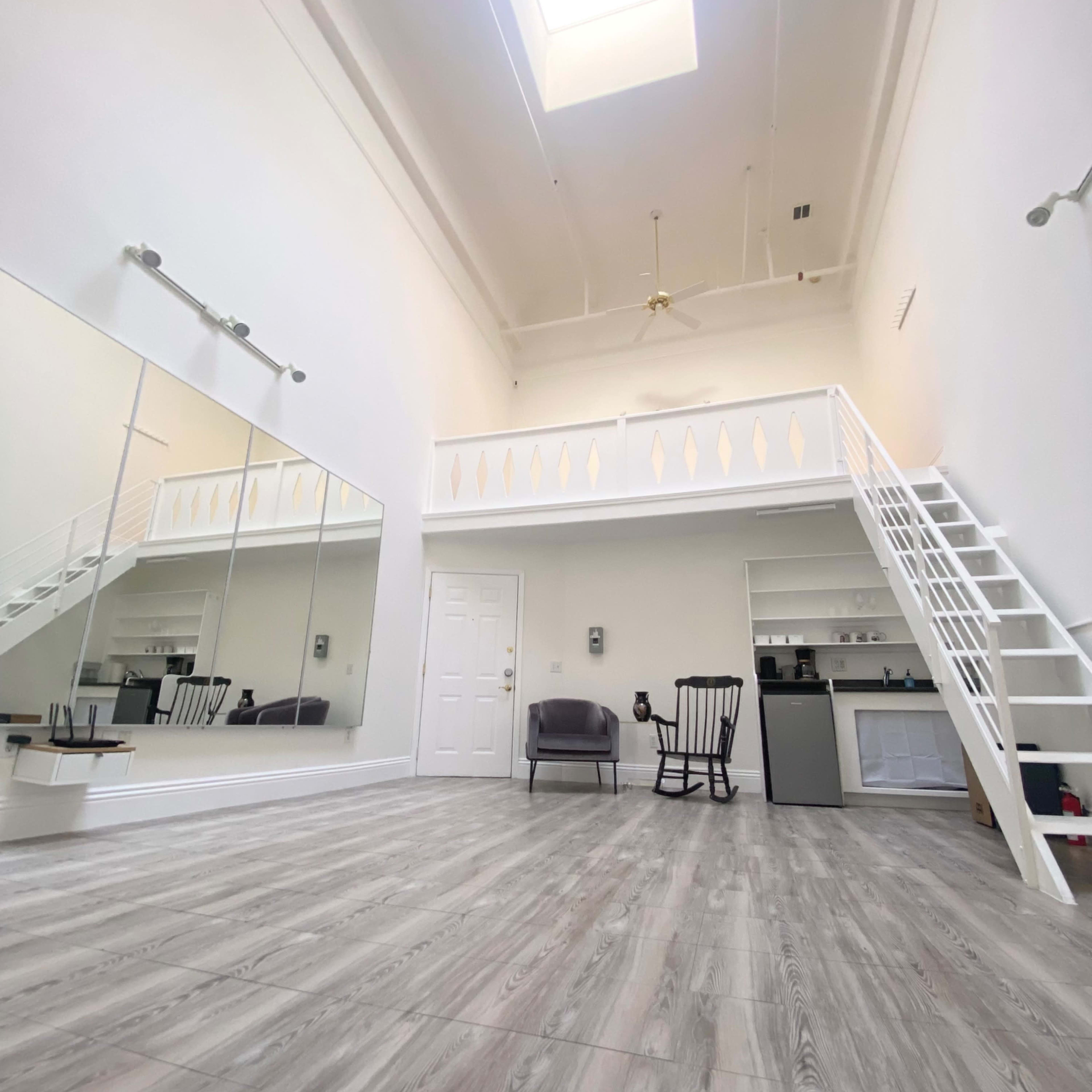 A spacious room with high ceilings, featuring a skylight, a mirror wall, and a small loft area with a staircase.