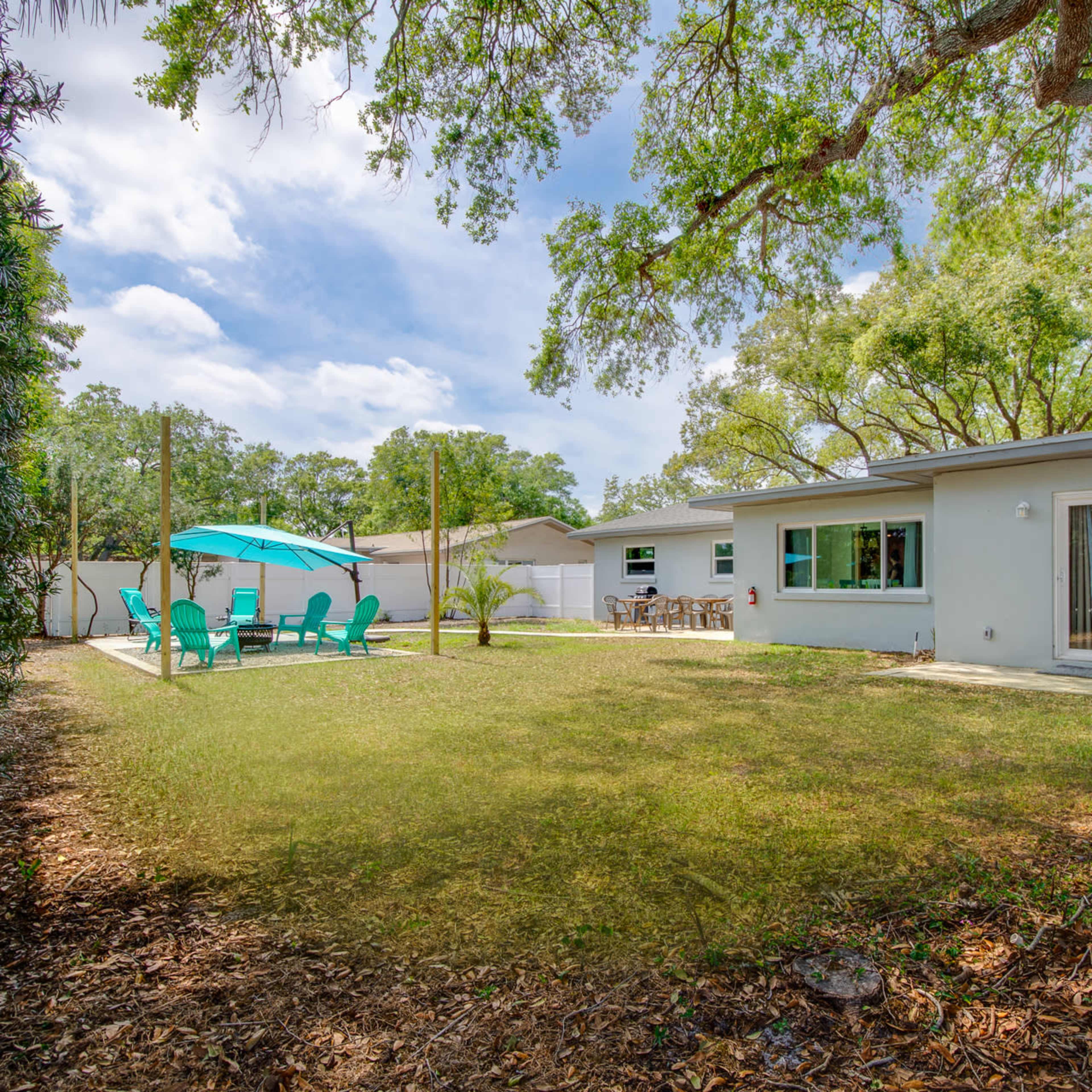 A spacious backyard with a green lawn, a patio area with chairs, and trees providing shade.