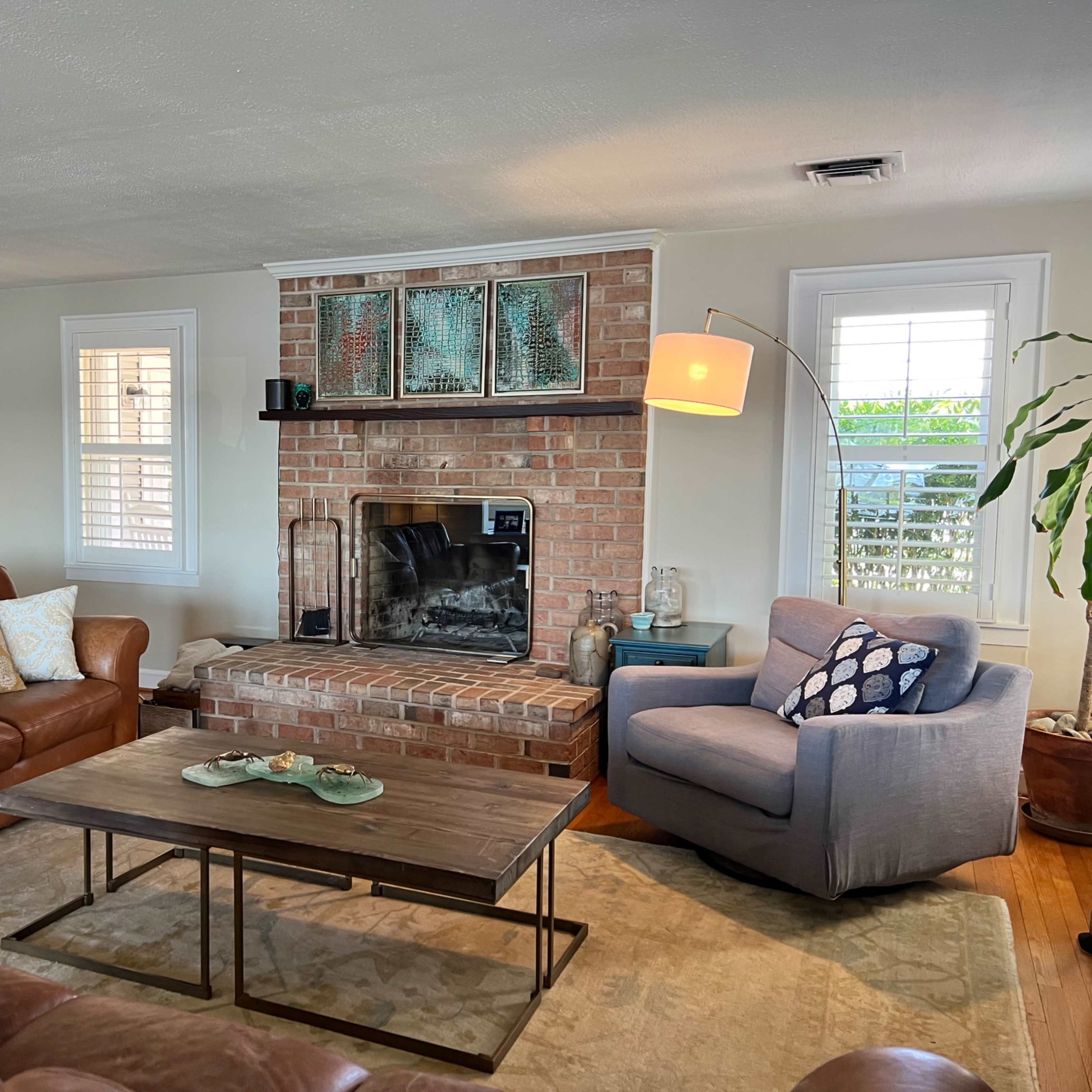 The living room features a brick fireplace, a leather sofa, an armchair, and a coffee table with decorative items.