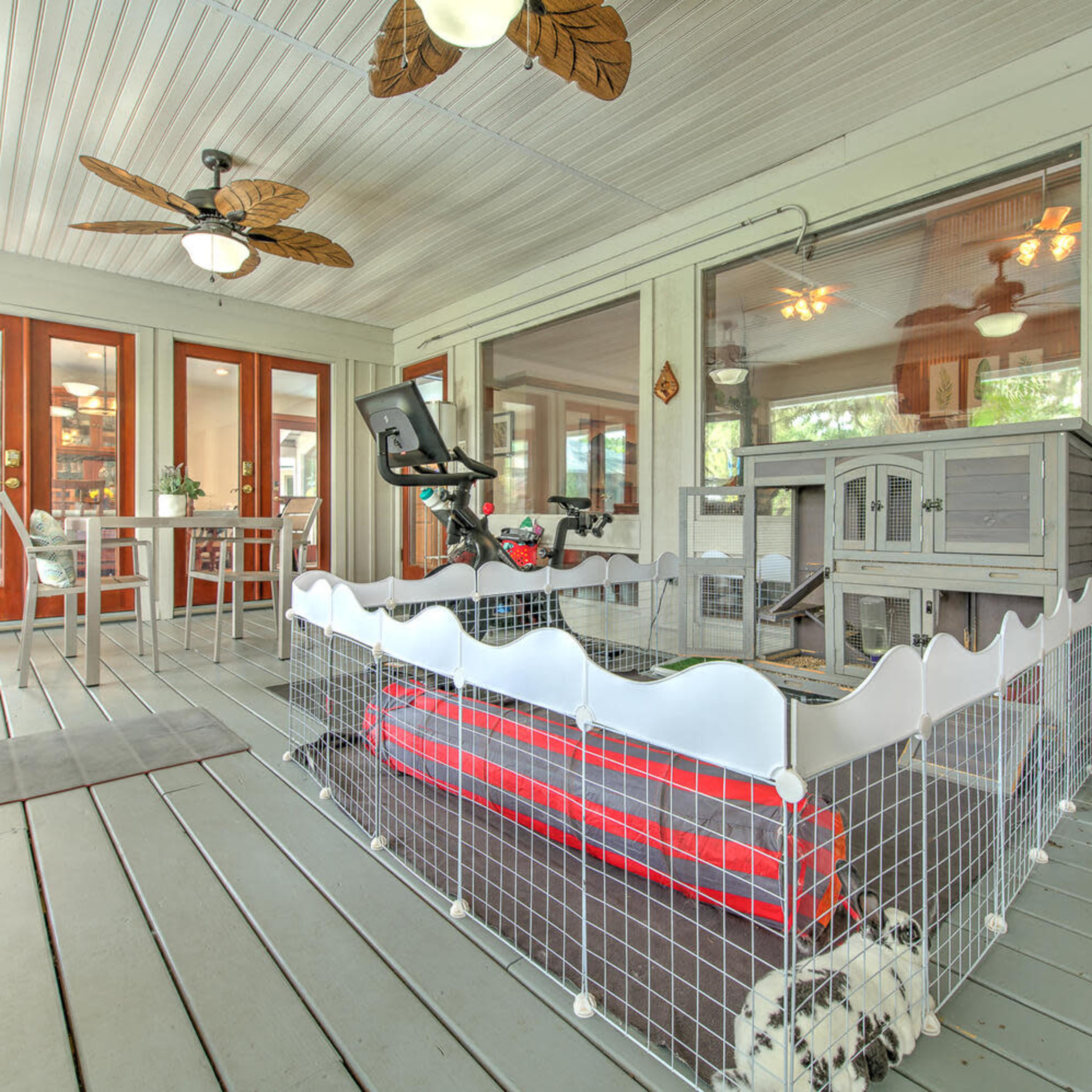 A playpen for a pet is set up on a covered porch with a dining table and chairs in the background.