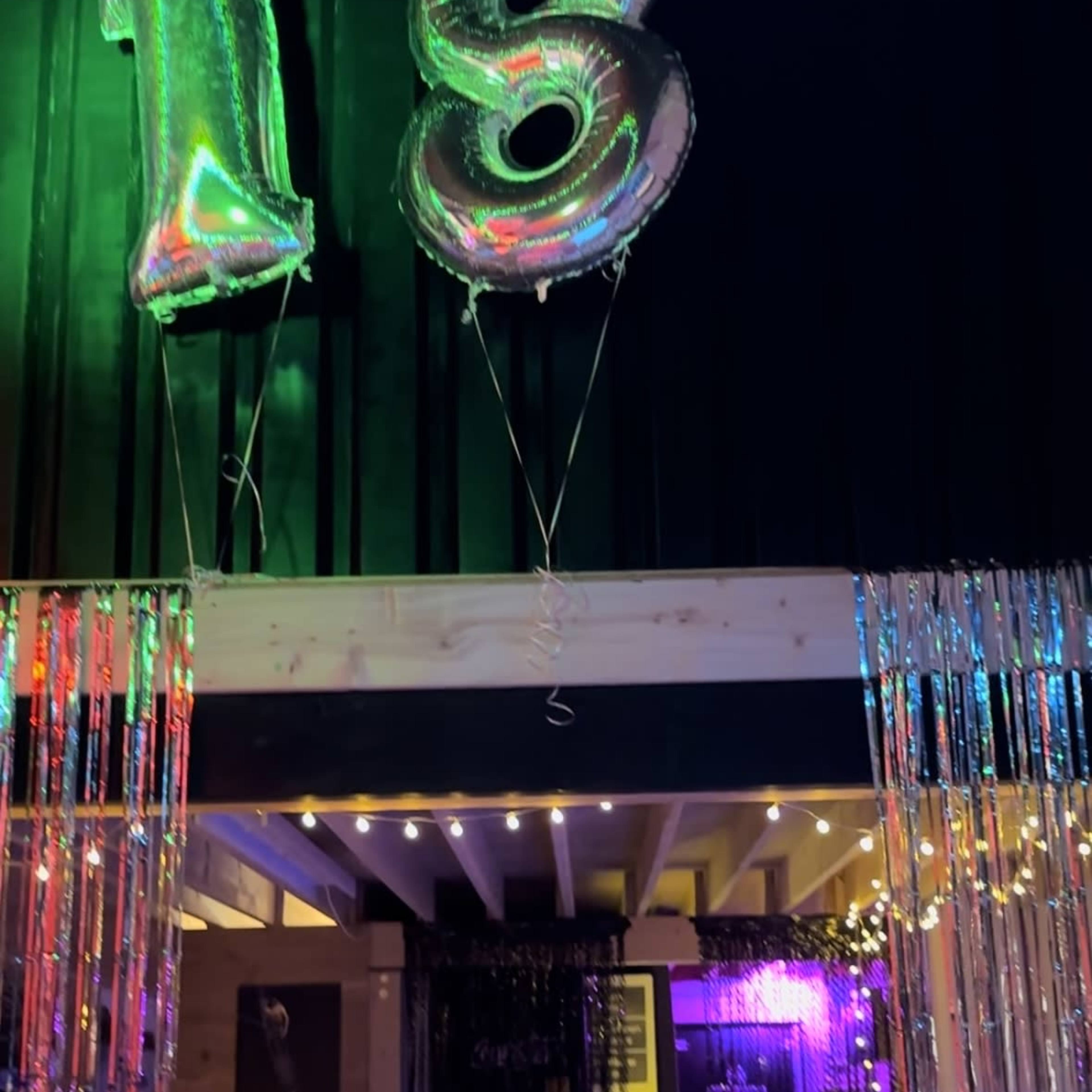 A decorated entrance with silver balloons reading "18" and colorful lights illuminating a party setting.