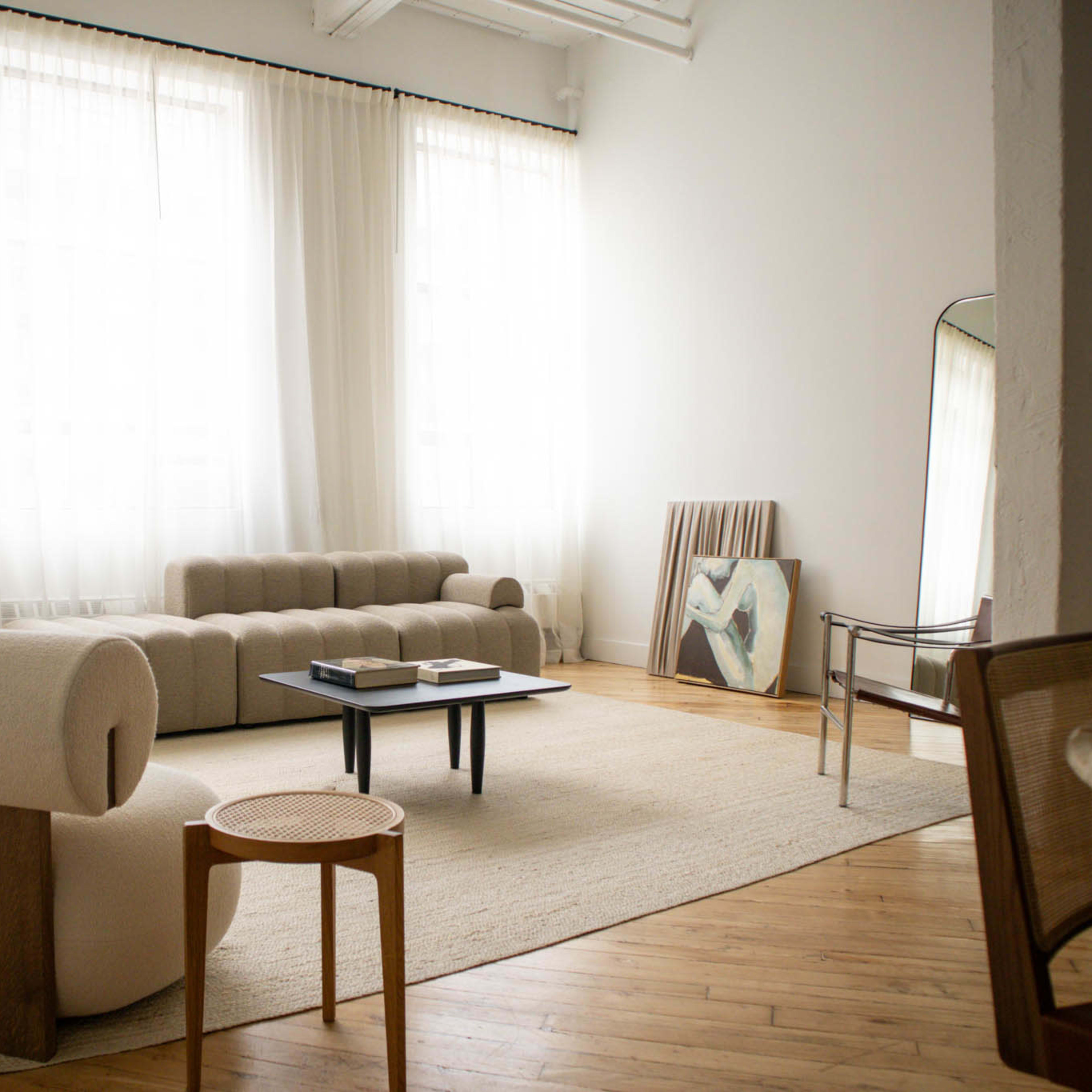 A spacious living room with large windows, two sofas, a coffee table, and a painting leaning against the wall.