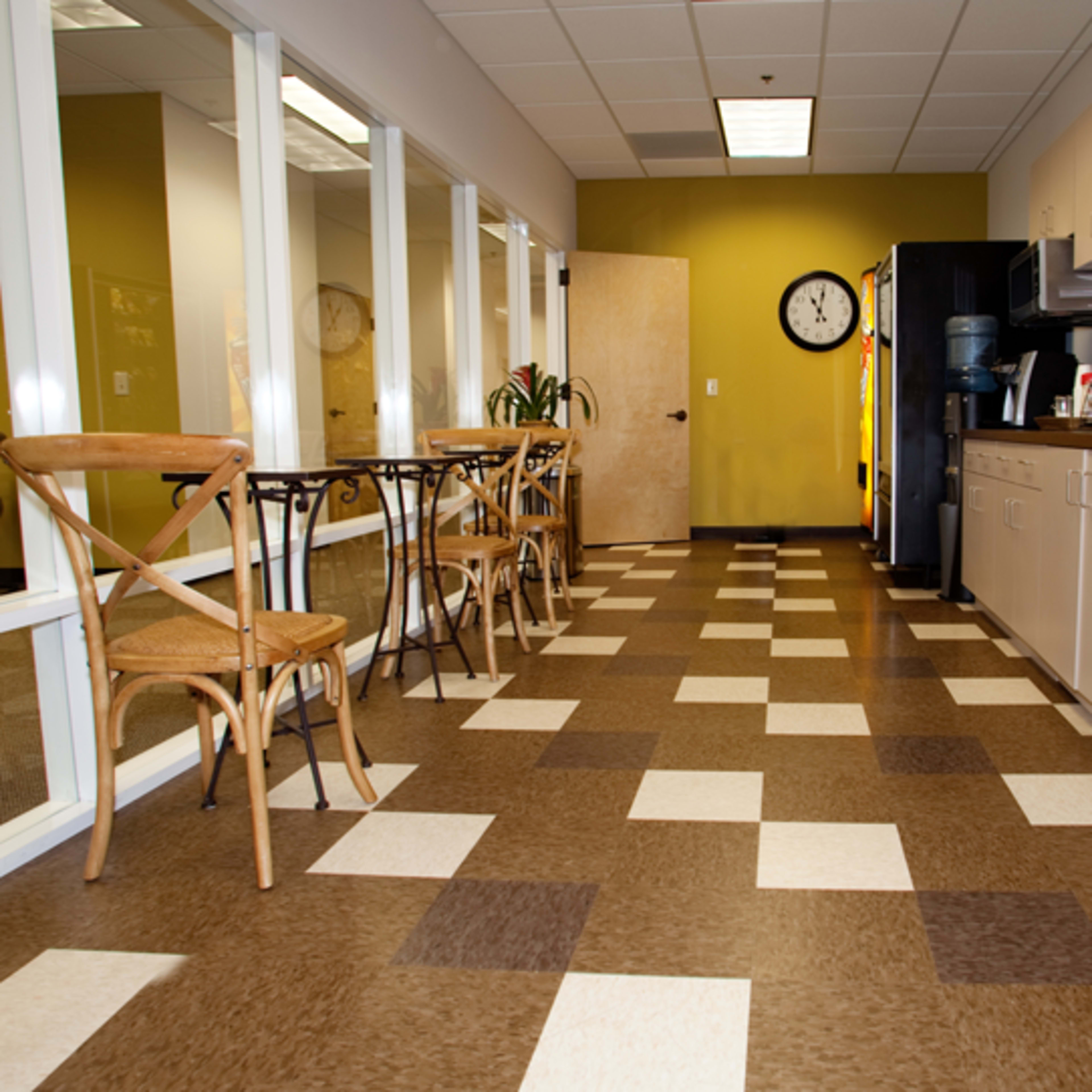 A kitchen area with a checkered floor, a dining table with chairs, and a refrigerator next to cabinets and a sink.