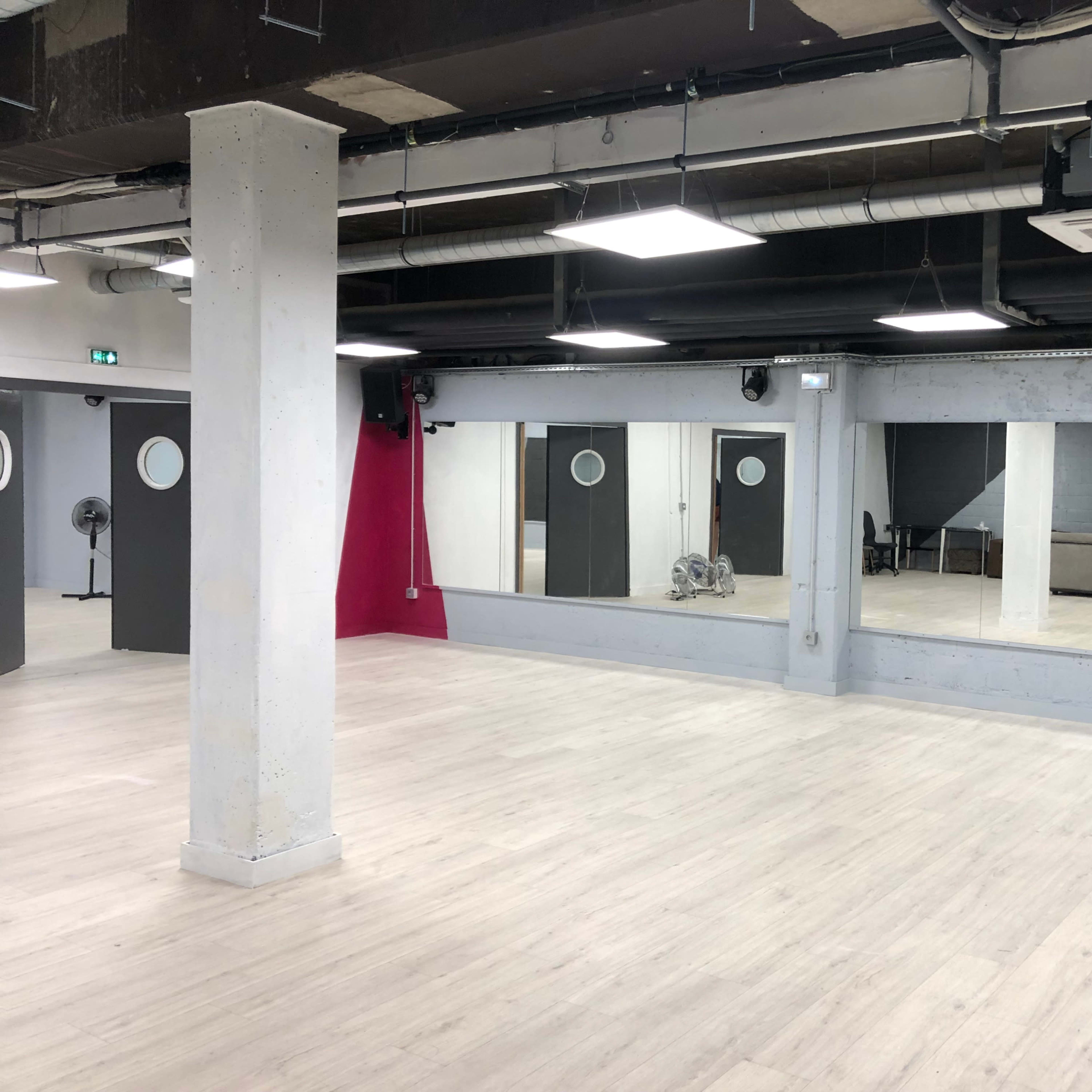 A spacious, empty studio with two large mirrors, gray walls, and separate doors, along with a staircase in the background.