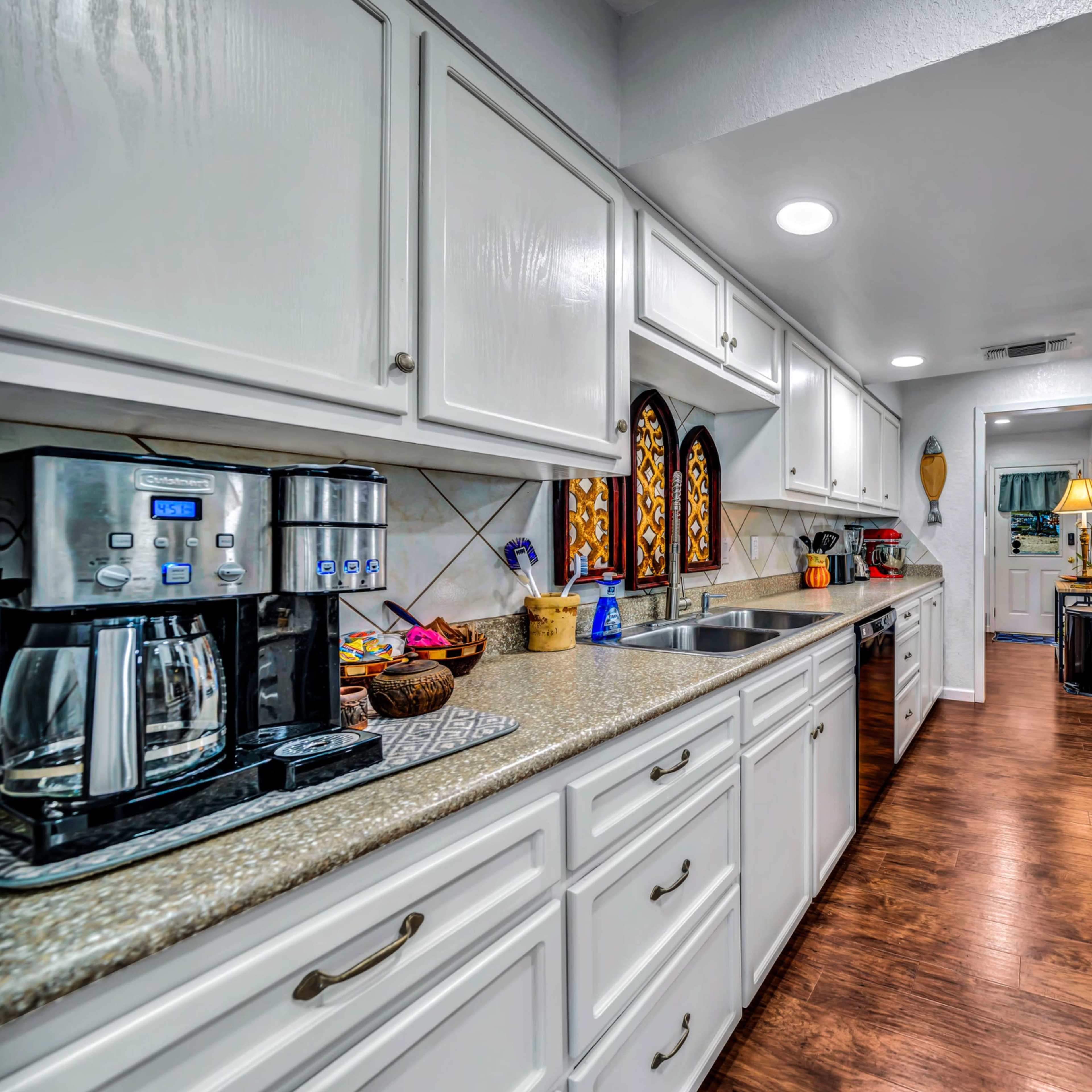 A modern kitchen with white cabinets, a coffee maker, and stainless steel appliances along a narrow layout.