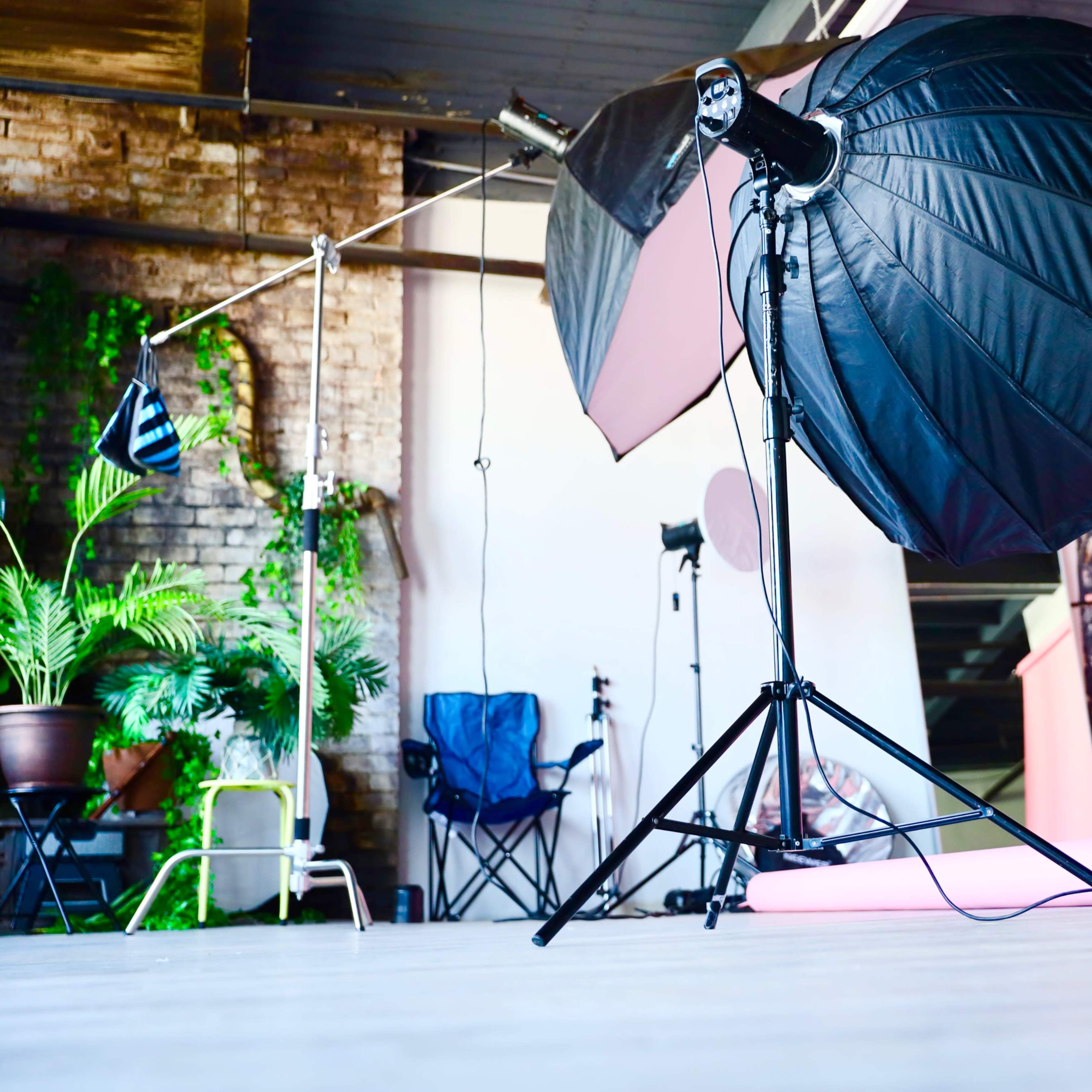 A photography studio with lighting equipment, a wooden stool, and a pink backdrop rolled on the floor.