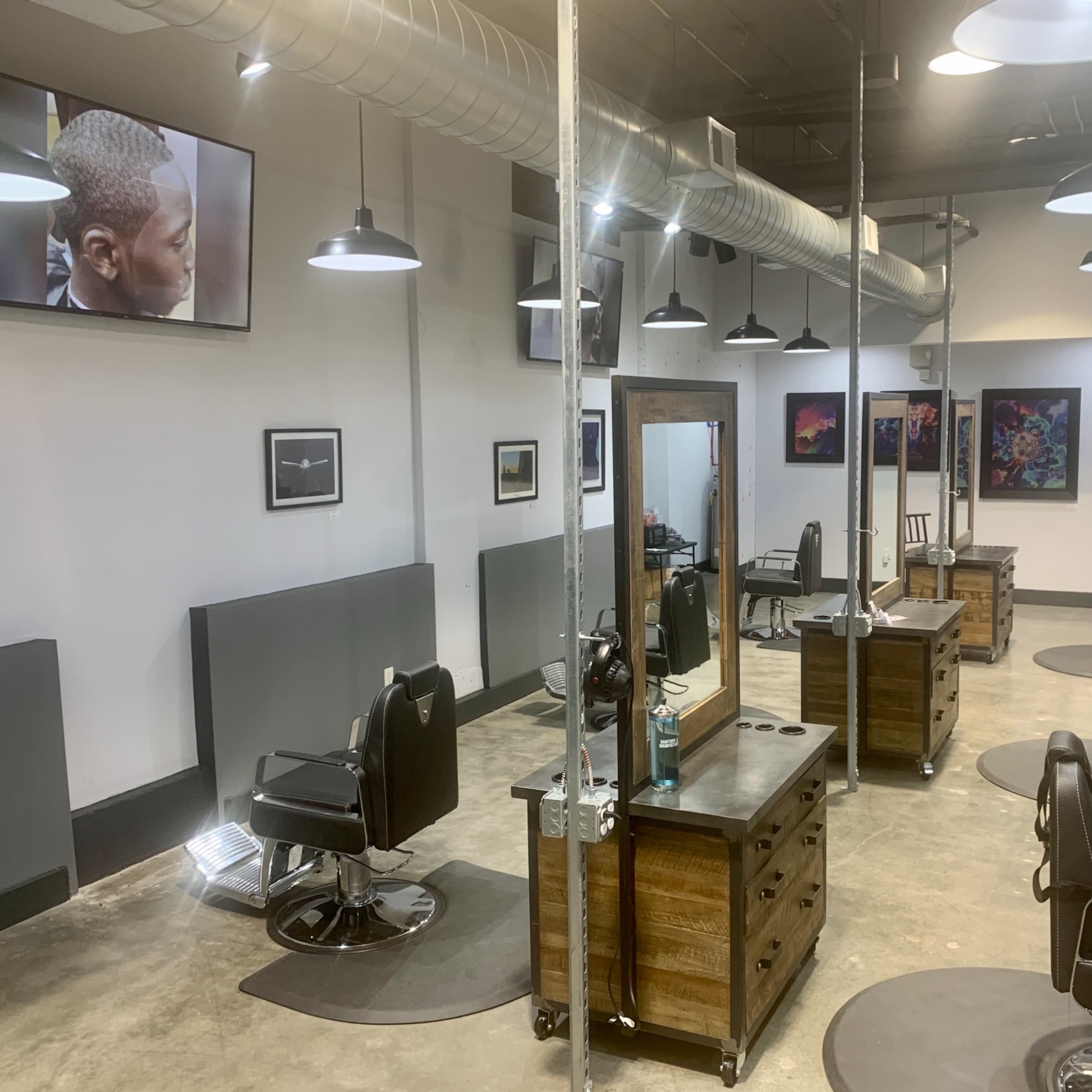 A modern hair salon features several styling stations with black chairs, large mirrors, and wall-mounted televisions displaying images.