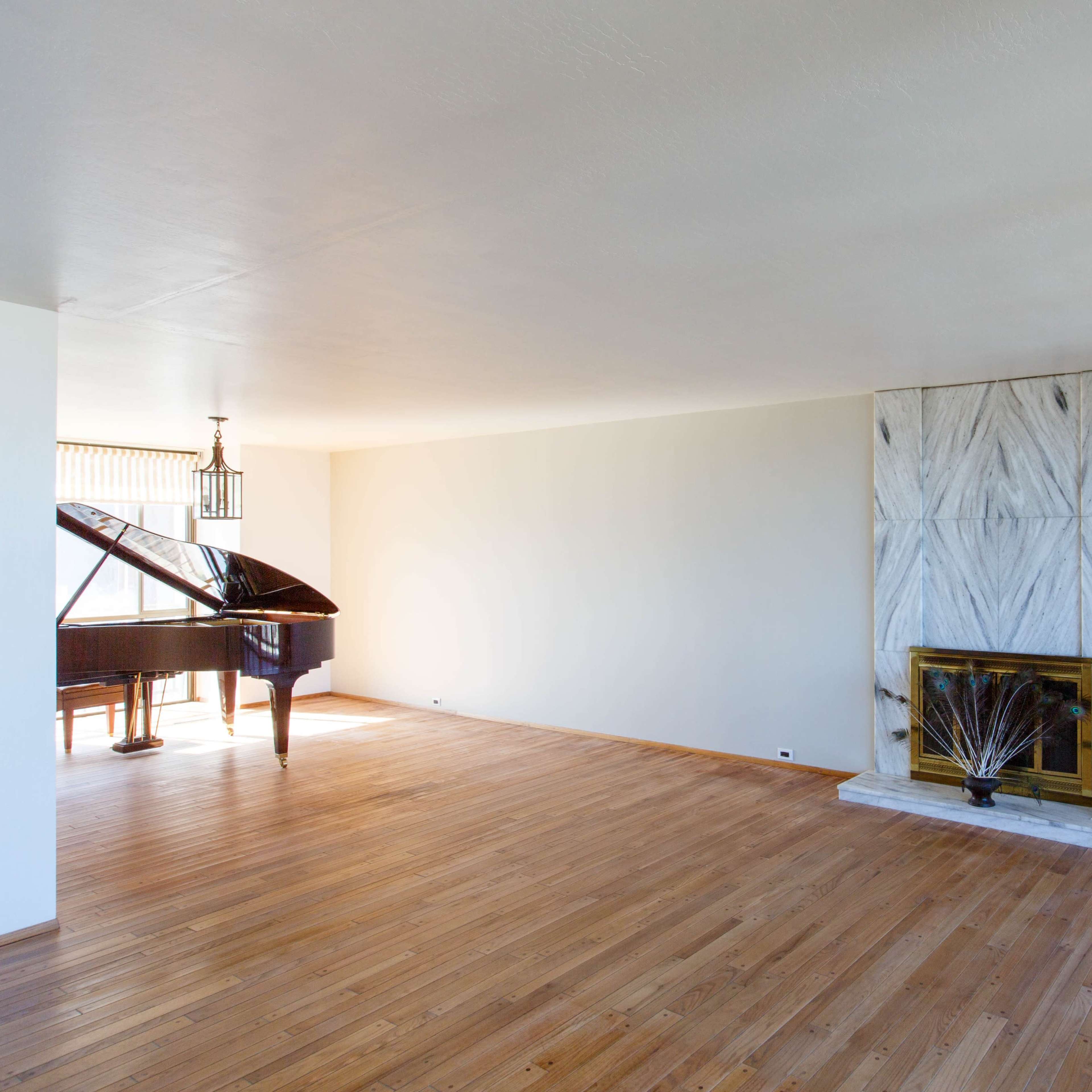 A spacious, empty room with a grand piano in one corner and a marble fireplace on one wall.