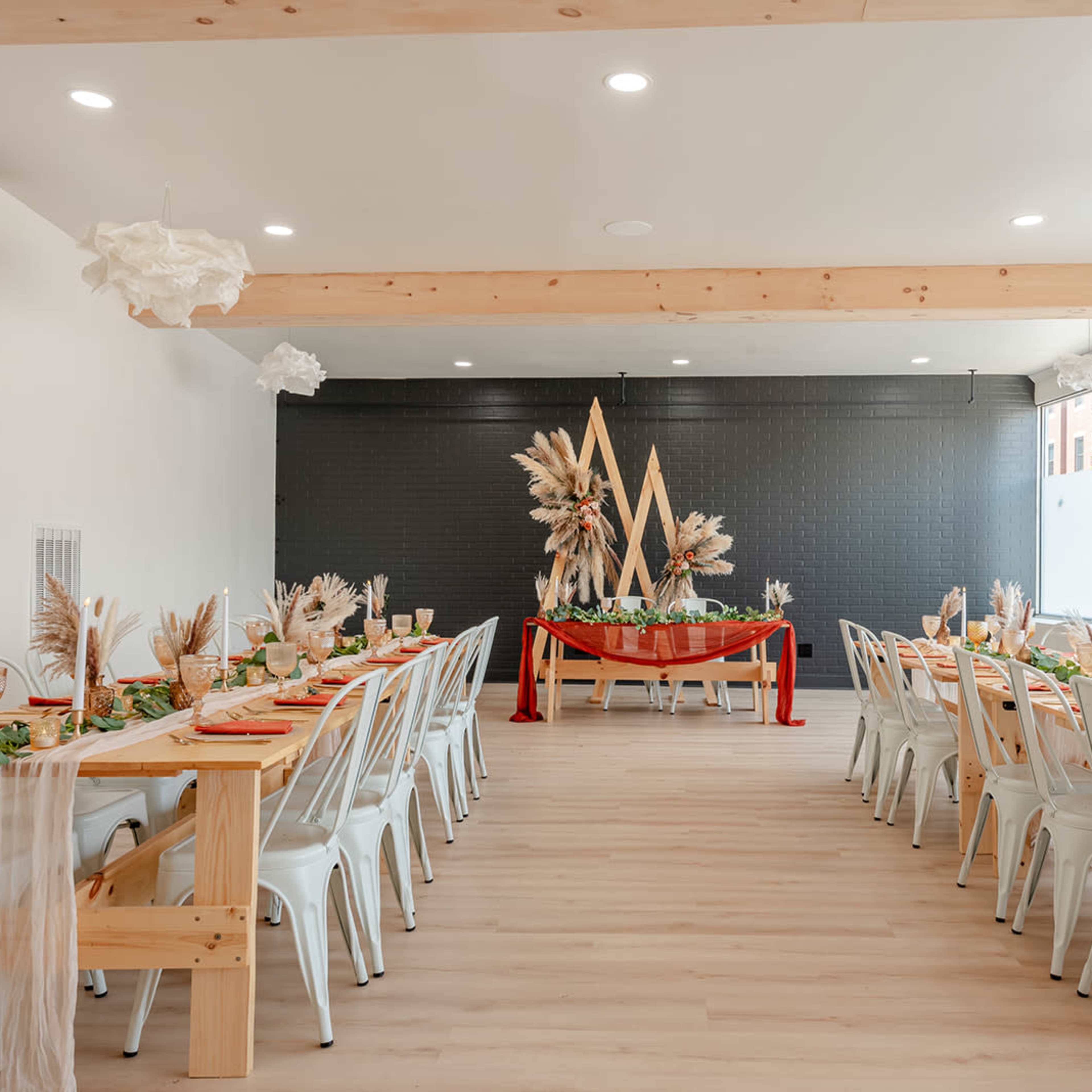 A light-filled dining room features long wooden tables set with decorative centerpieces and elegant table settings.