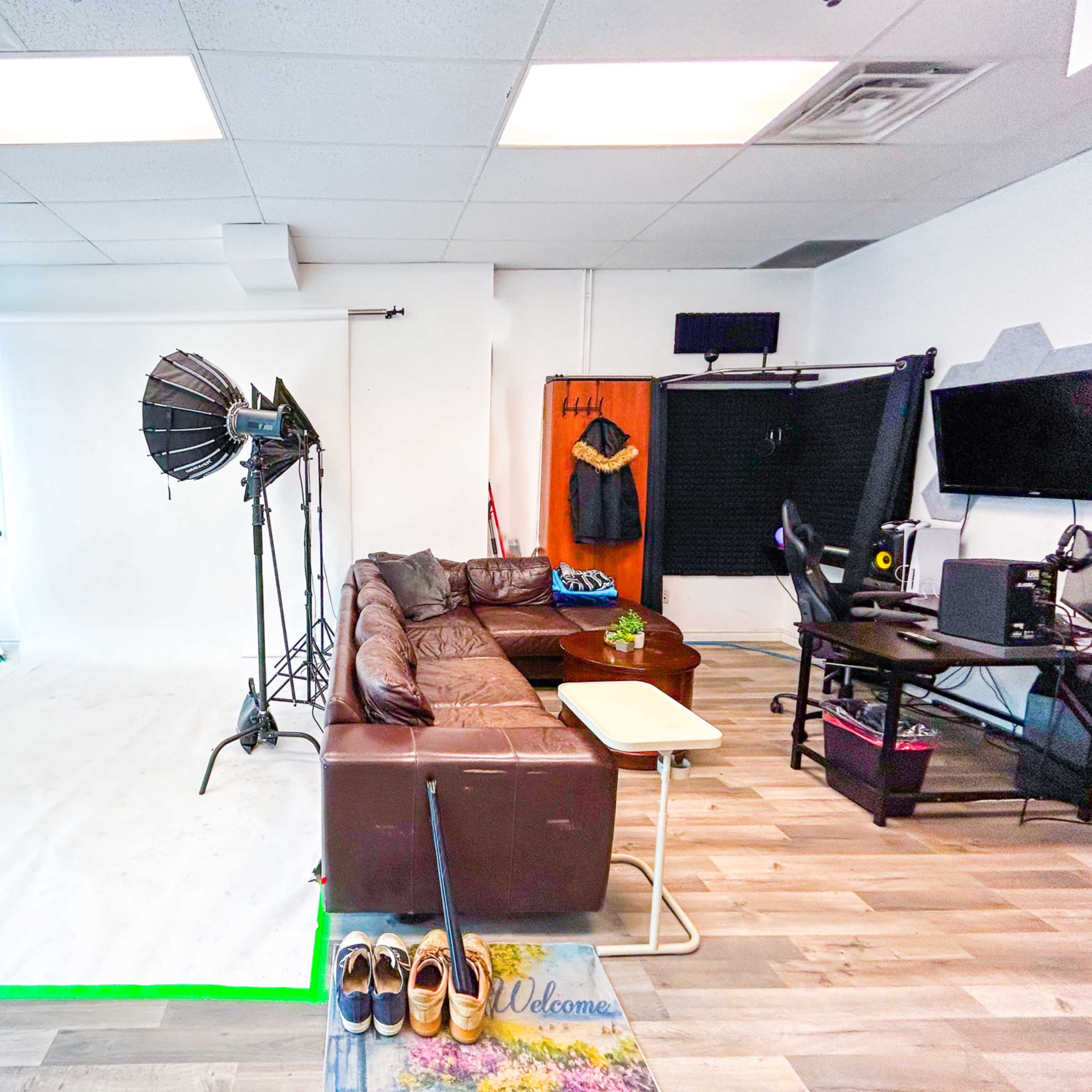 A photography studio with a white backdrop, lighting equipment, a brown couch, a small table, and a computer setup.
