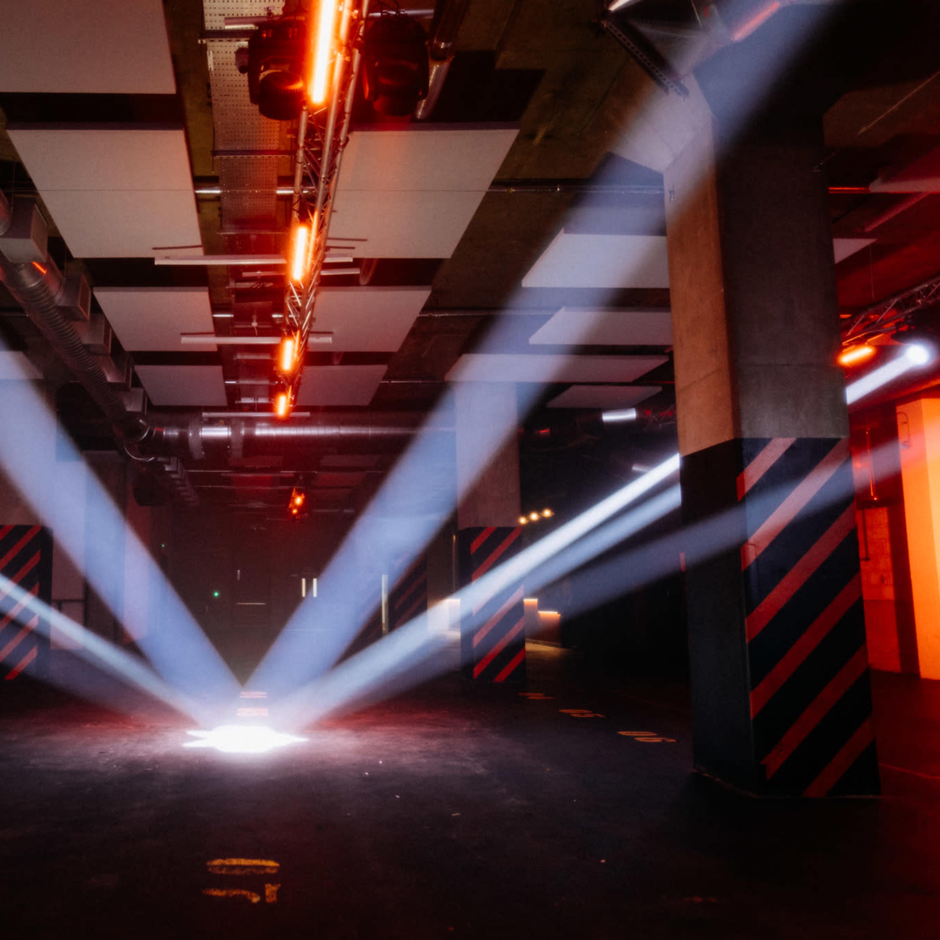 A large, dimly lit industrial space featuring beams of light shining down from the ceiling onto a central area.