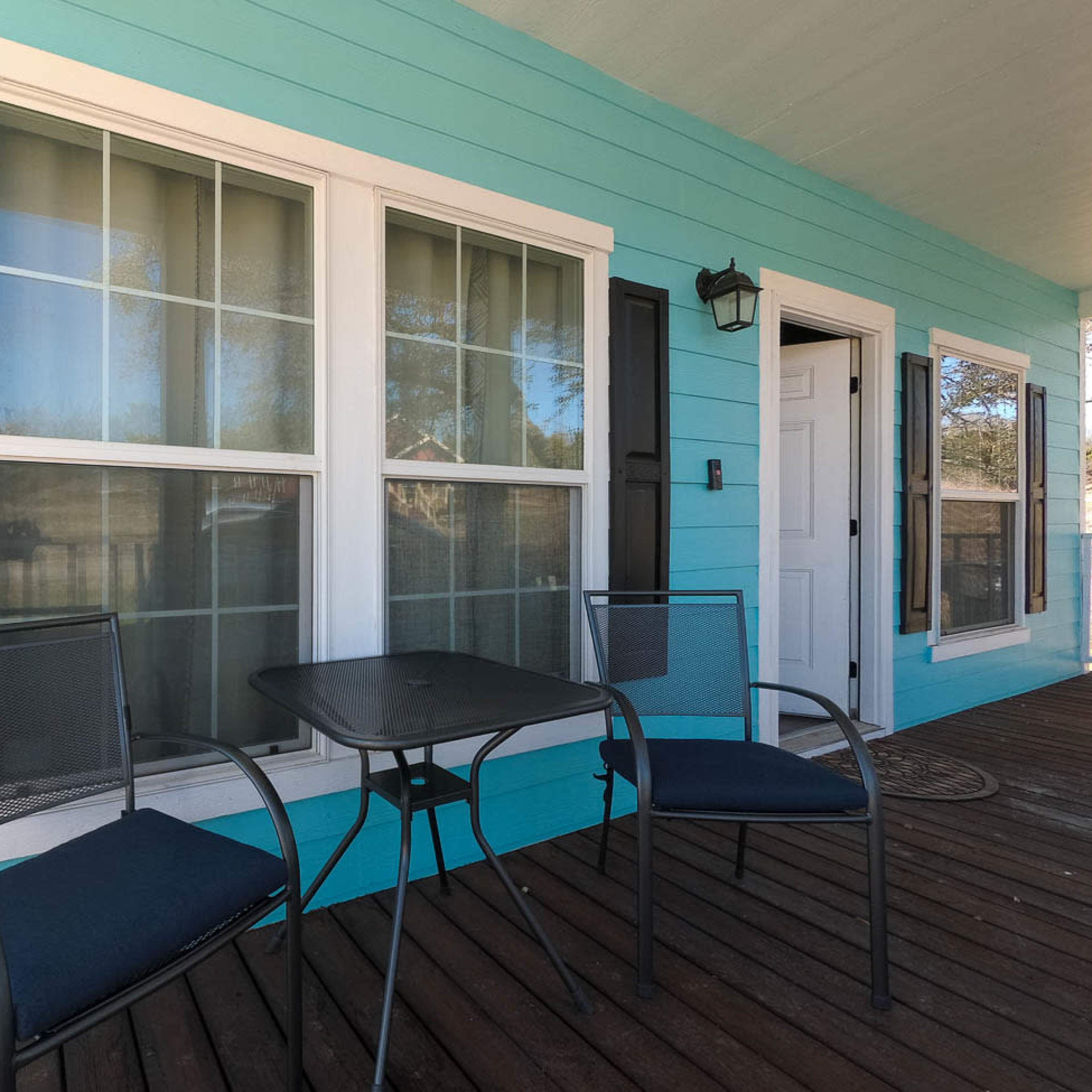 A porch with two chairs and a small table in front of two large windows, all set against a bright blue wall.