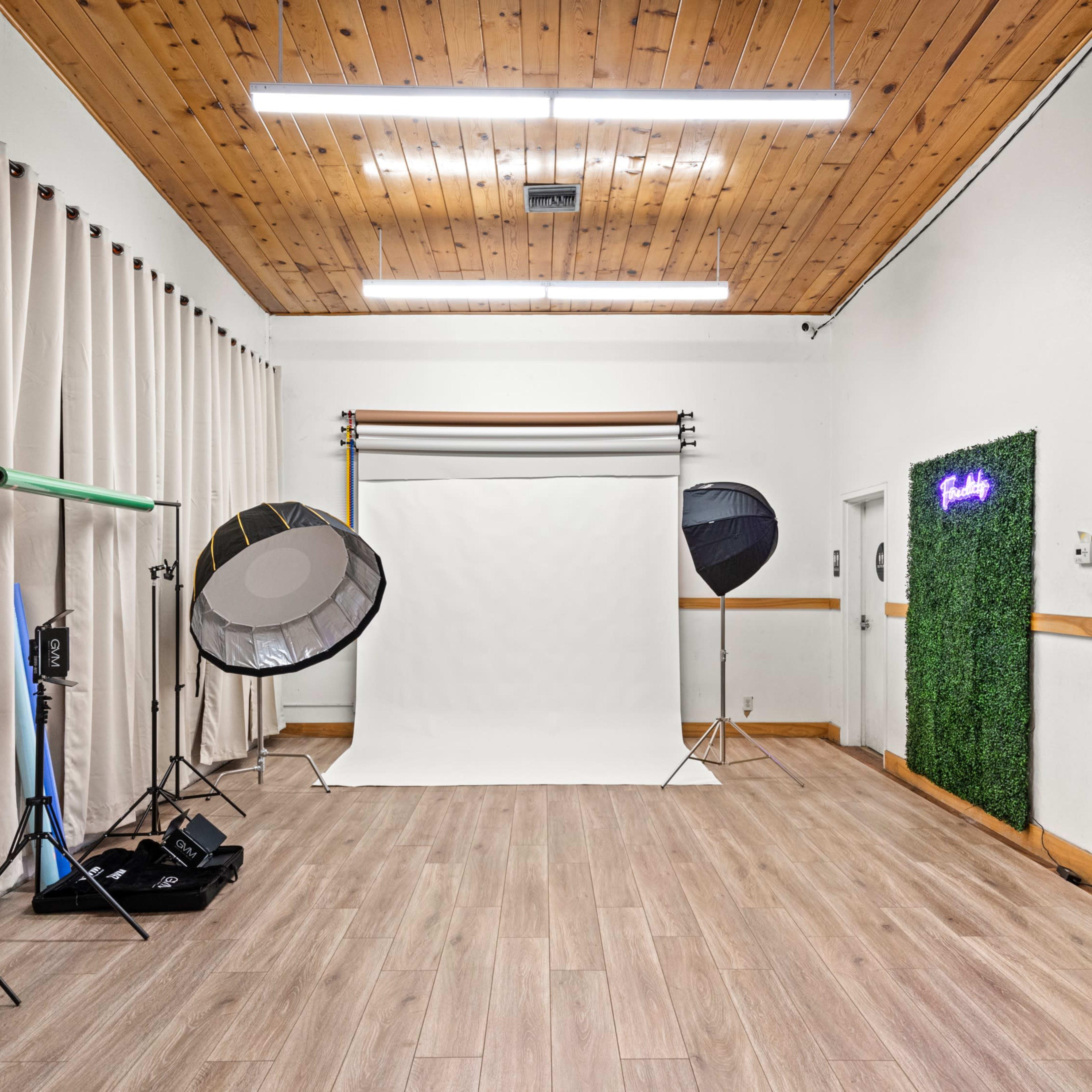 A photography studio with a white backdrop, lighting equipment, and a small Christmas tree in the corner.