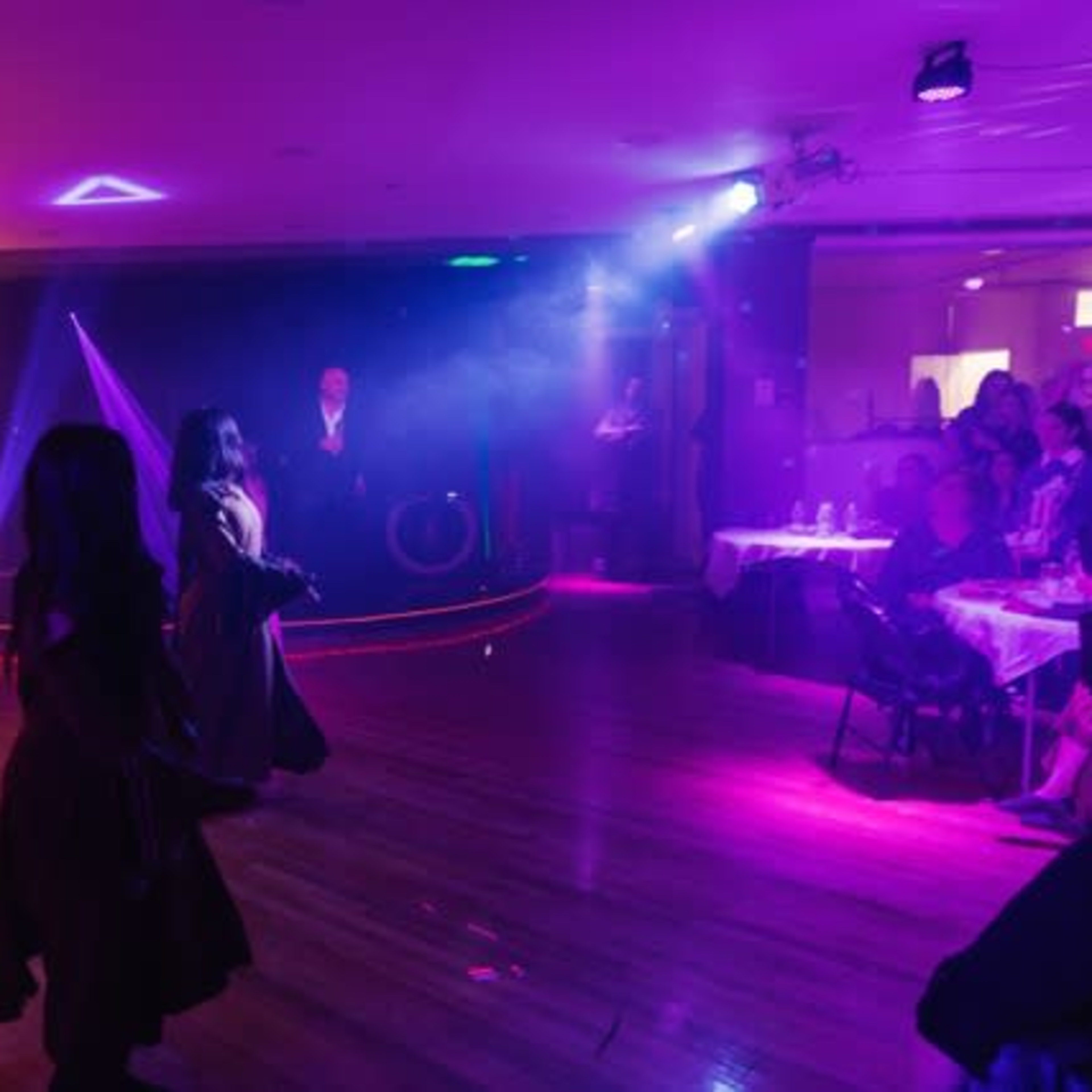 A group of dancers perform on a stage with colorful lighting in a venue filled with seated spectators.