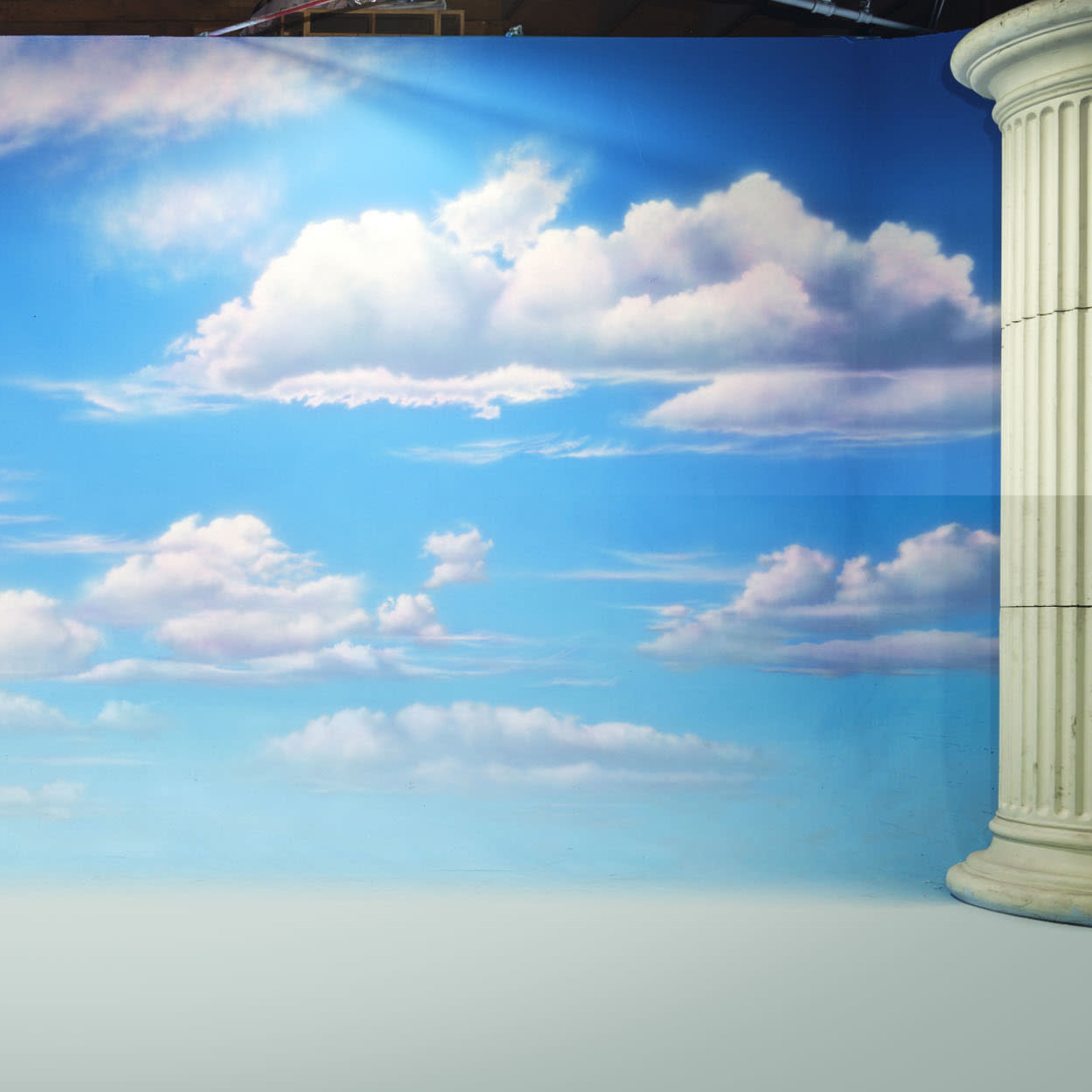 A painted backdrop of a blue sky adorned with fluffy white clouds.
