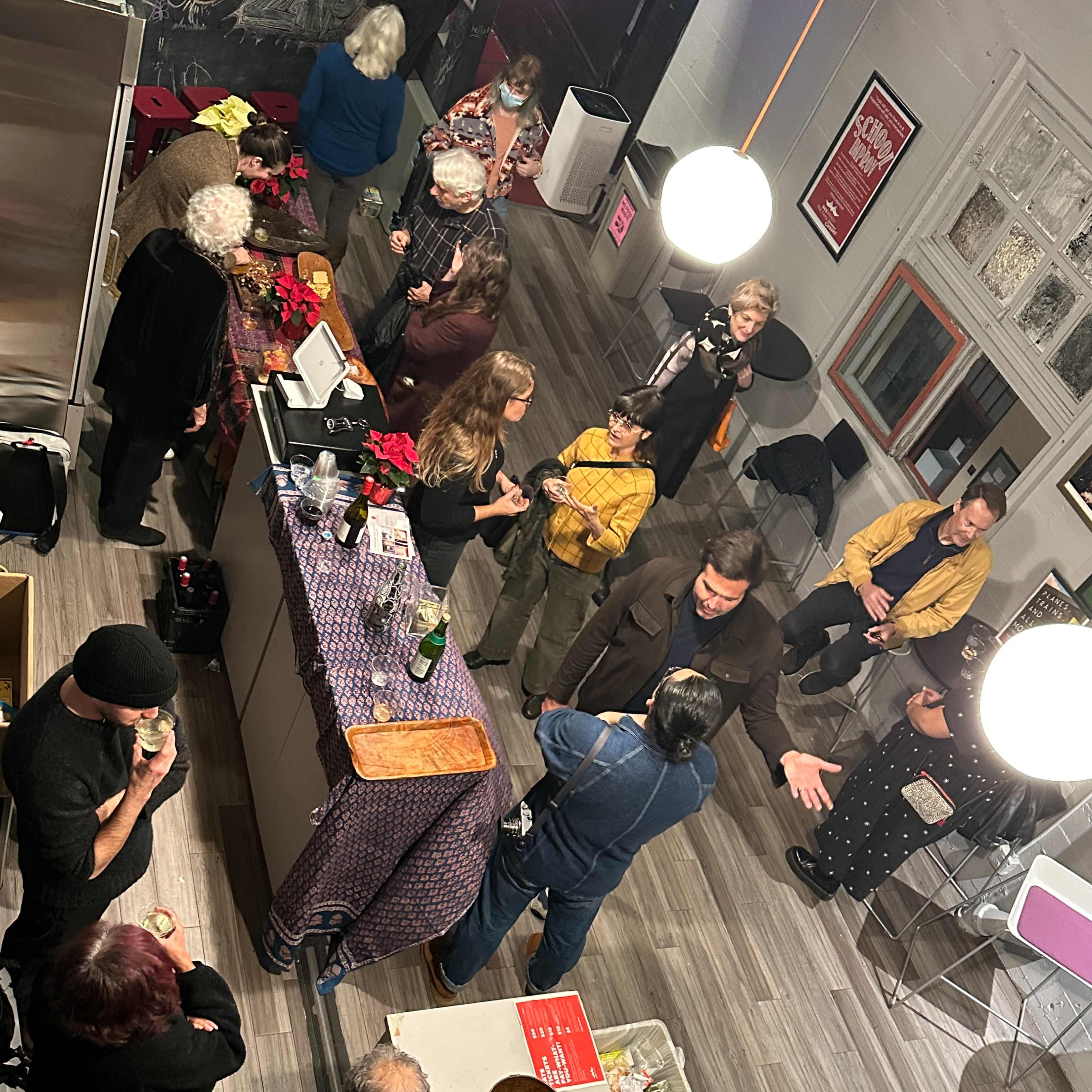 A lively gathering of people socializing around a bar area with drinks and snacks in a spacious, well-lit room.