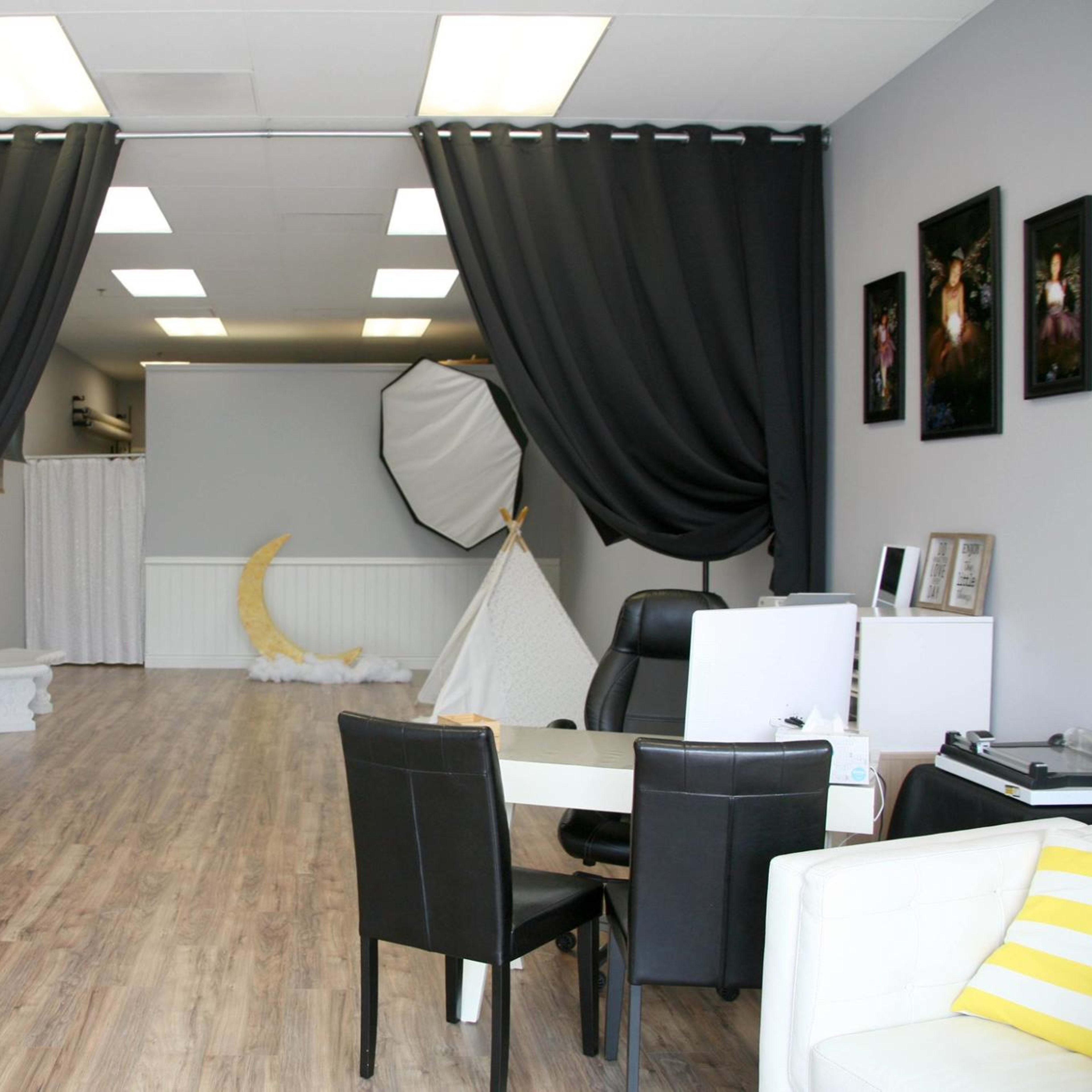 A spacious photography studio with grey walls, black curtains, and various photography props arranged throughout.
