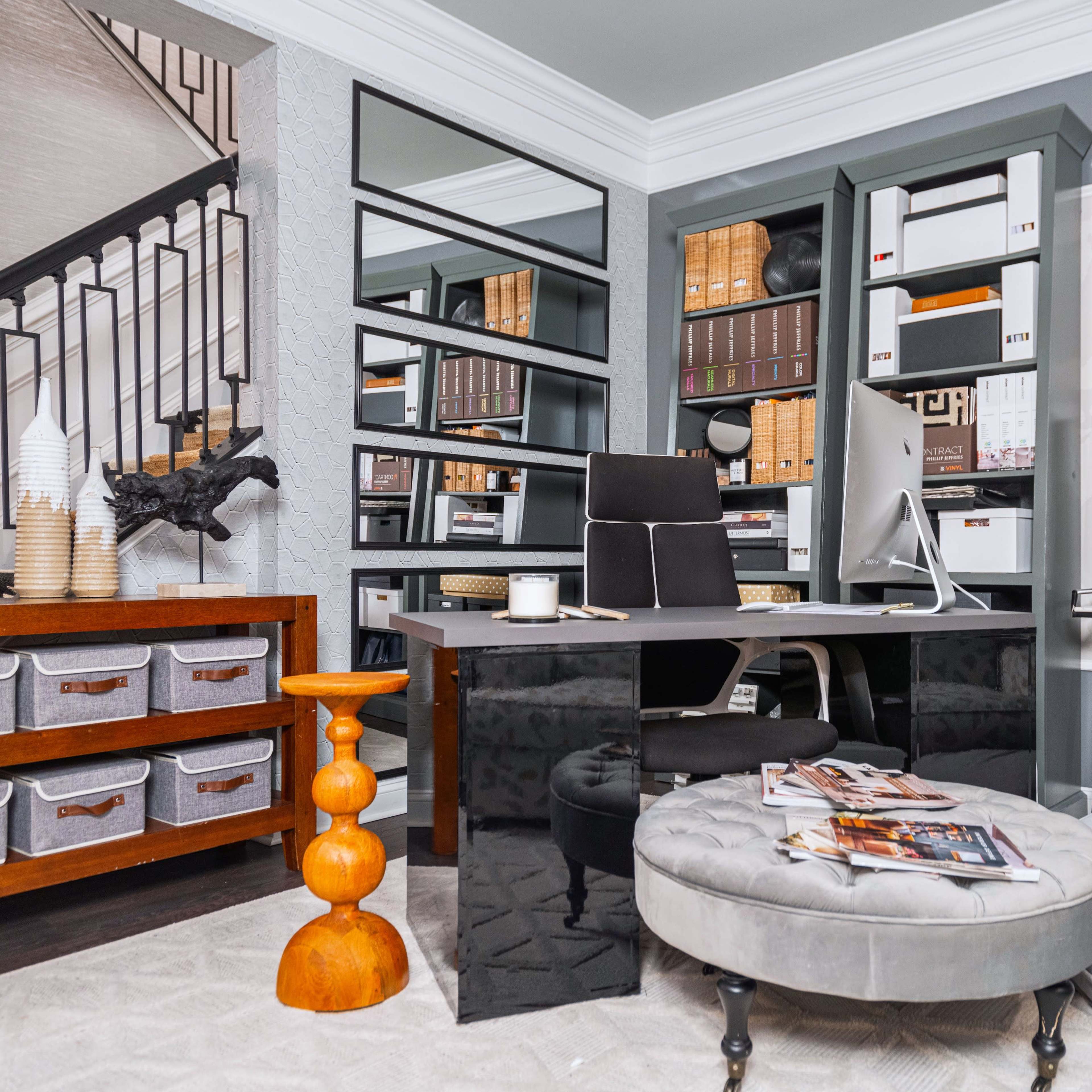 A stylish home office featuring a sleek black desk, organized storage boxes, a modern chair, and a staircase in a well-decorated space.