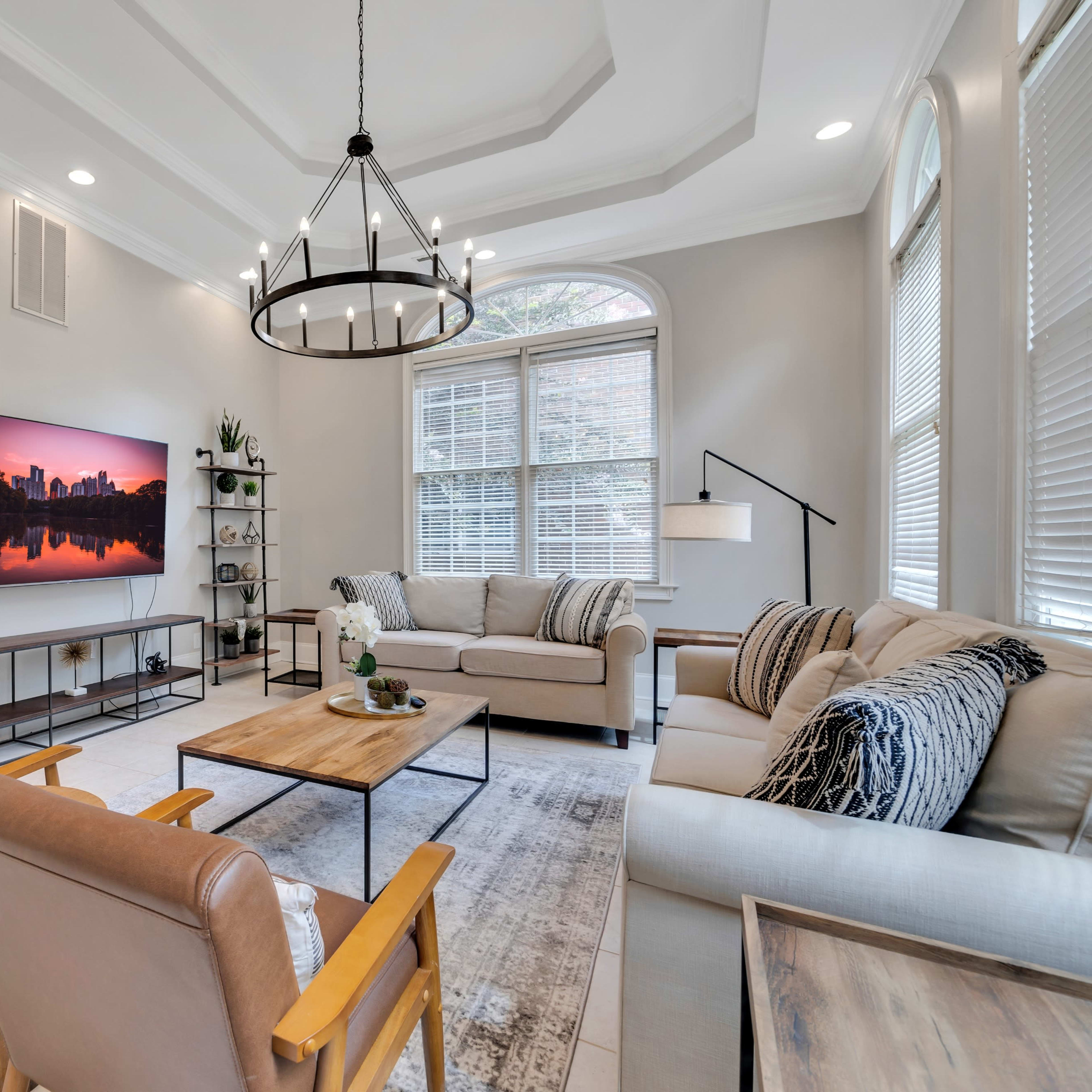 A modern living room with two brown armchairs, a light-colored sofa, a large television mounted on the wall, and a coffee table surrounded by decorative elements and plants.