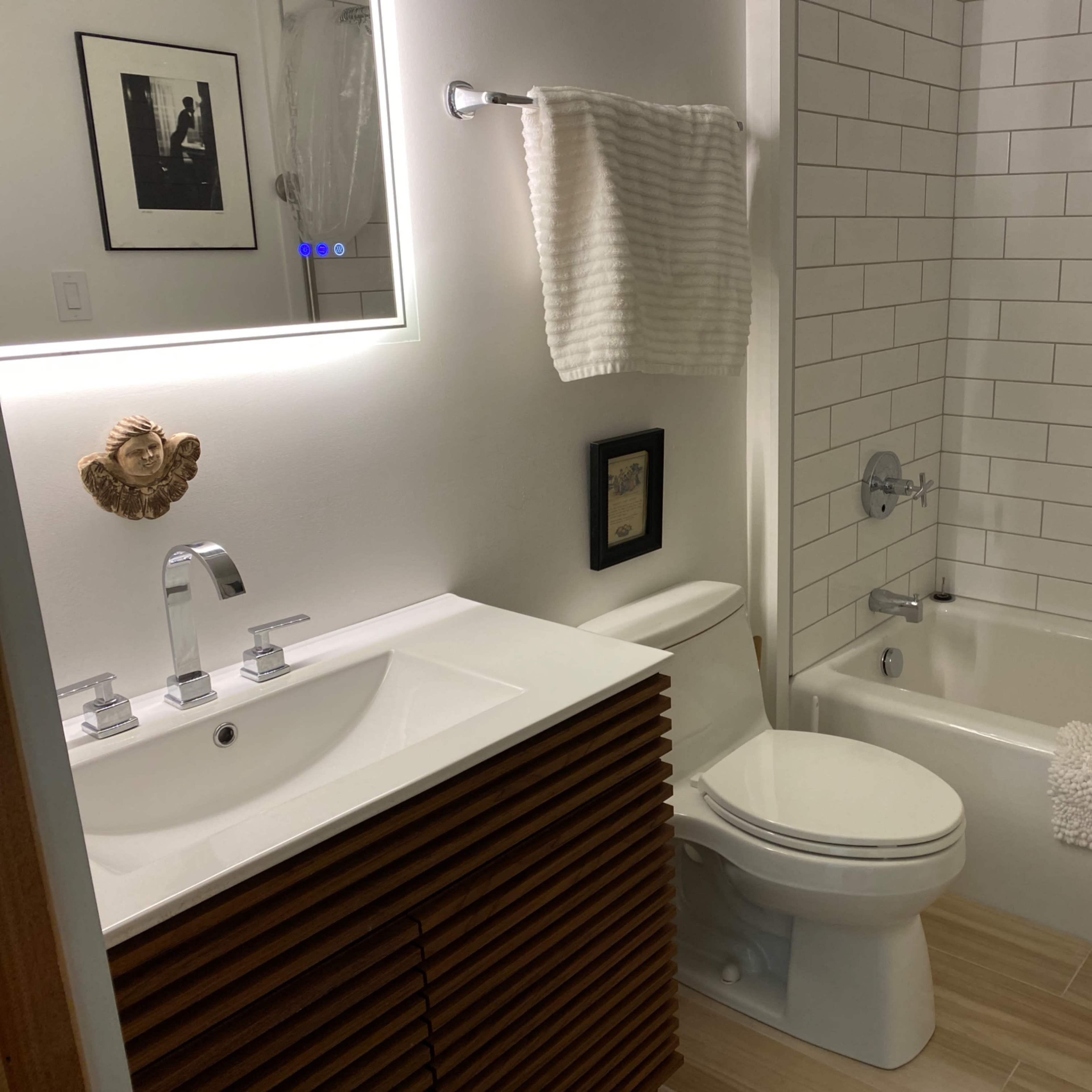 A modern bathroom featuring a white tiled wall, a bathtub with a shower, a wooden vanity with a sink, and a wall-mounted mirror.