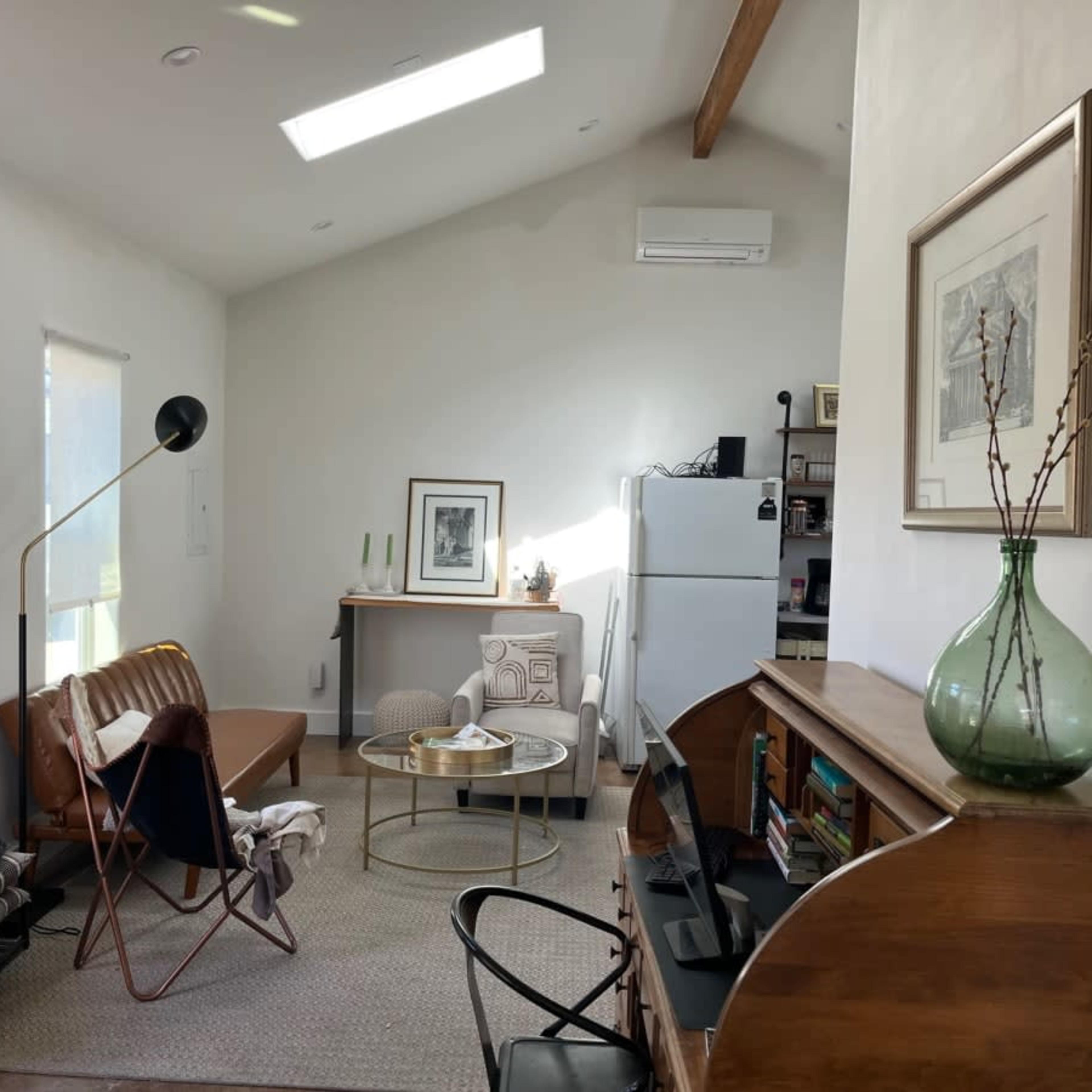 A cozy living space featuring a sofa, a coffee table, and a wooden cabinet, with large windows and a bright ceiling.