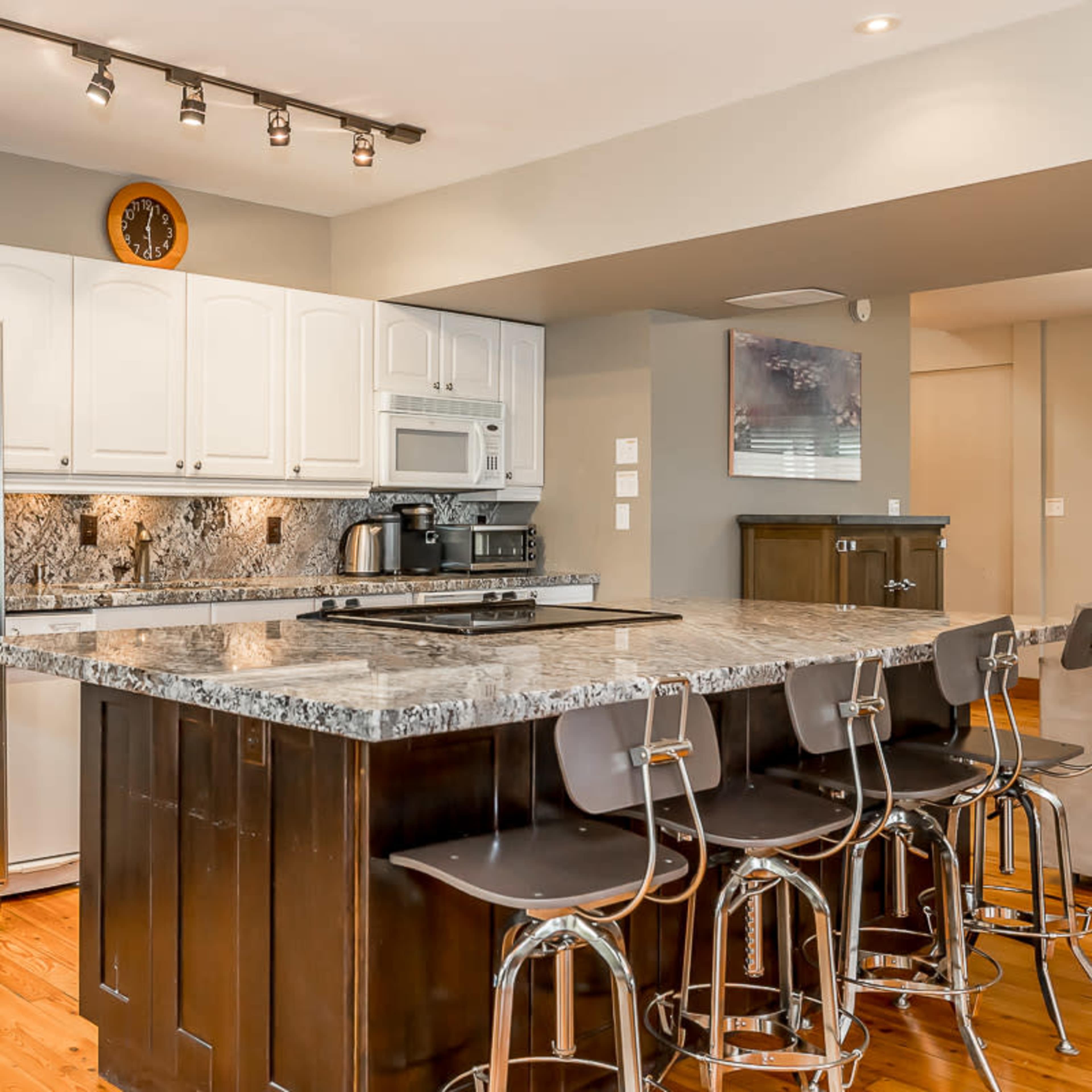 A modern kitchen with white cabinets, a large marble countertop, stainless steel appliances, and seating at the island.