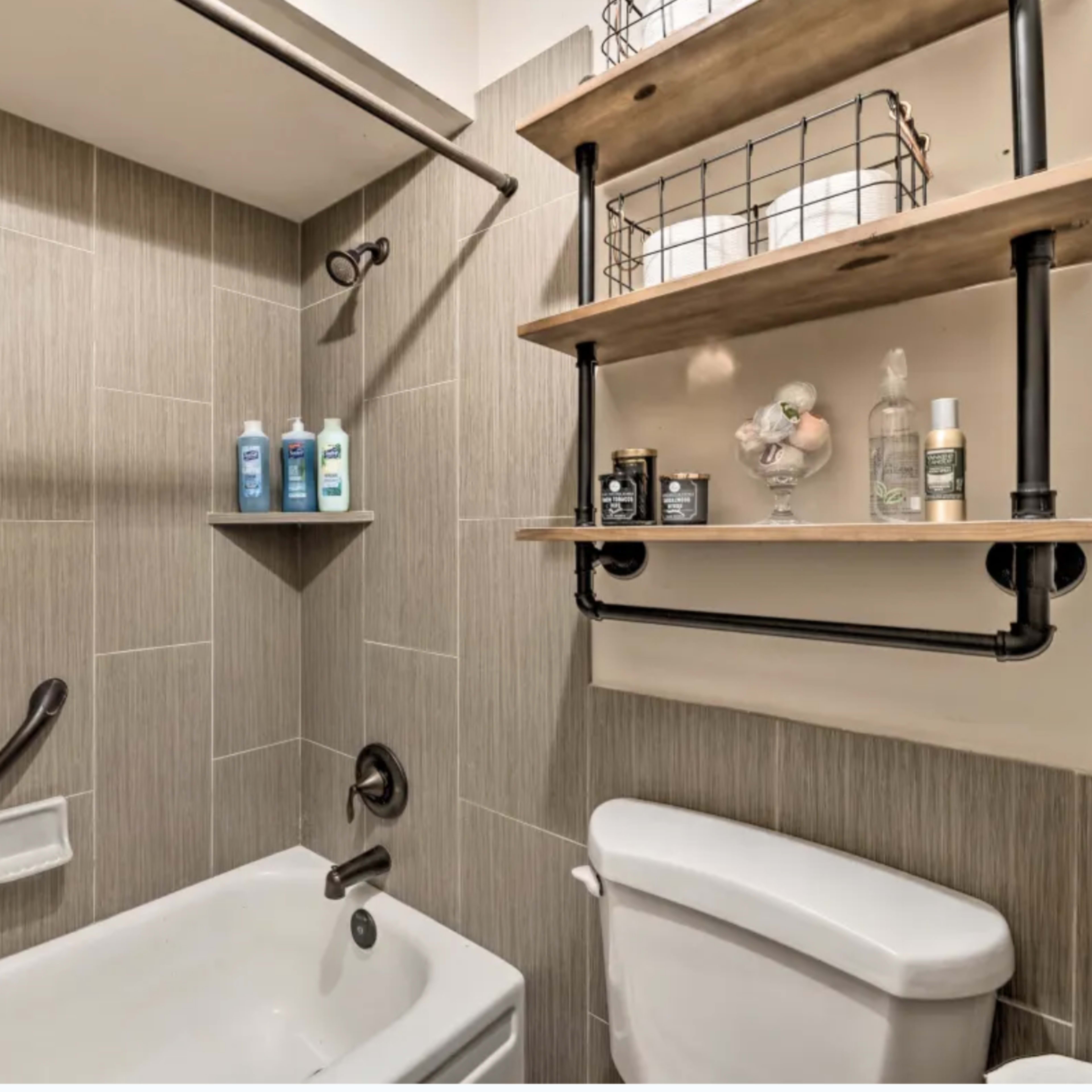 A bathroom with a bathtub, a wall shelf made of wood and metal, and a tiled mosaic accent.