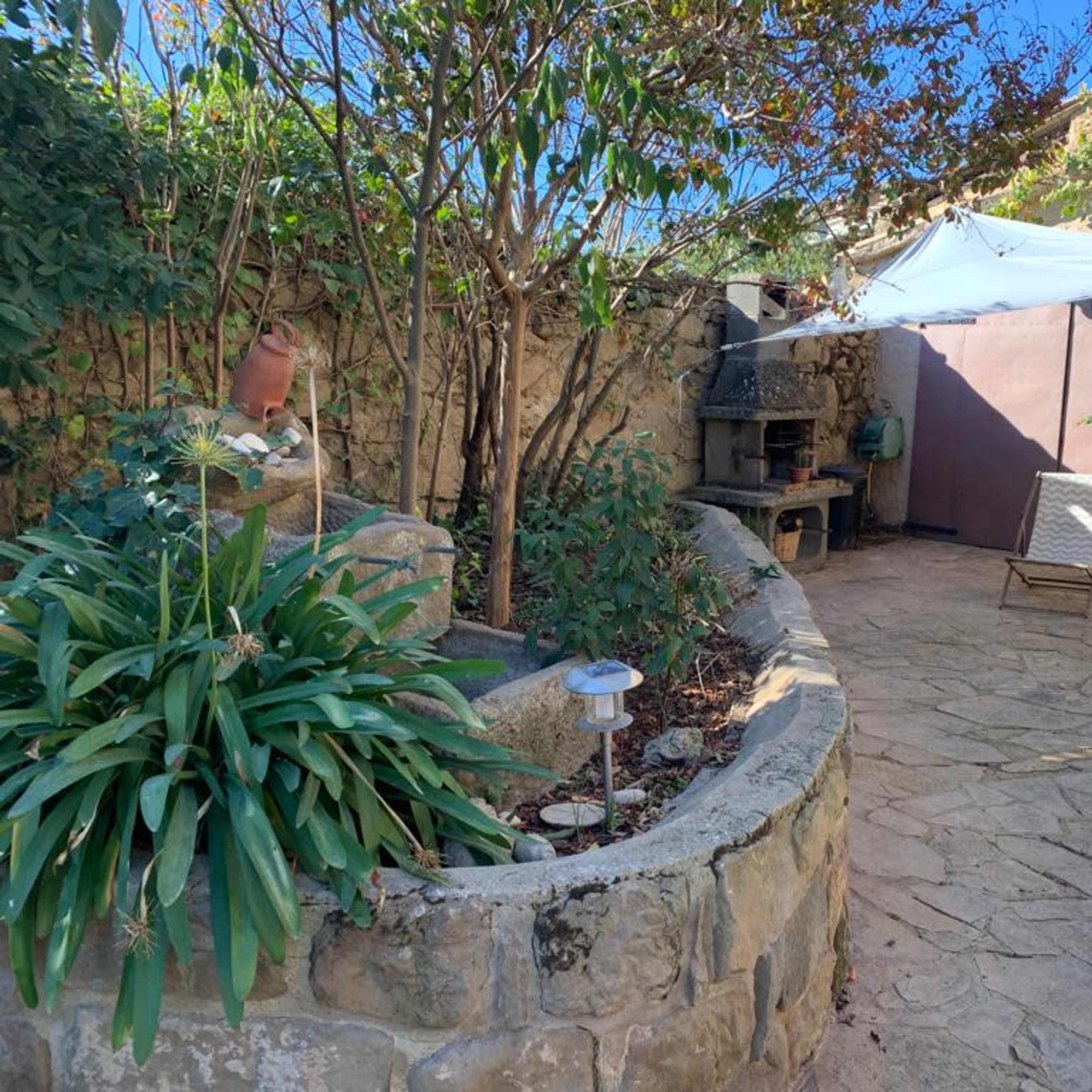 A stone-paved garden area featuring a seating space, a stone wall, and a shaded section with a white canopy.