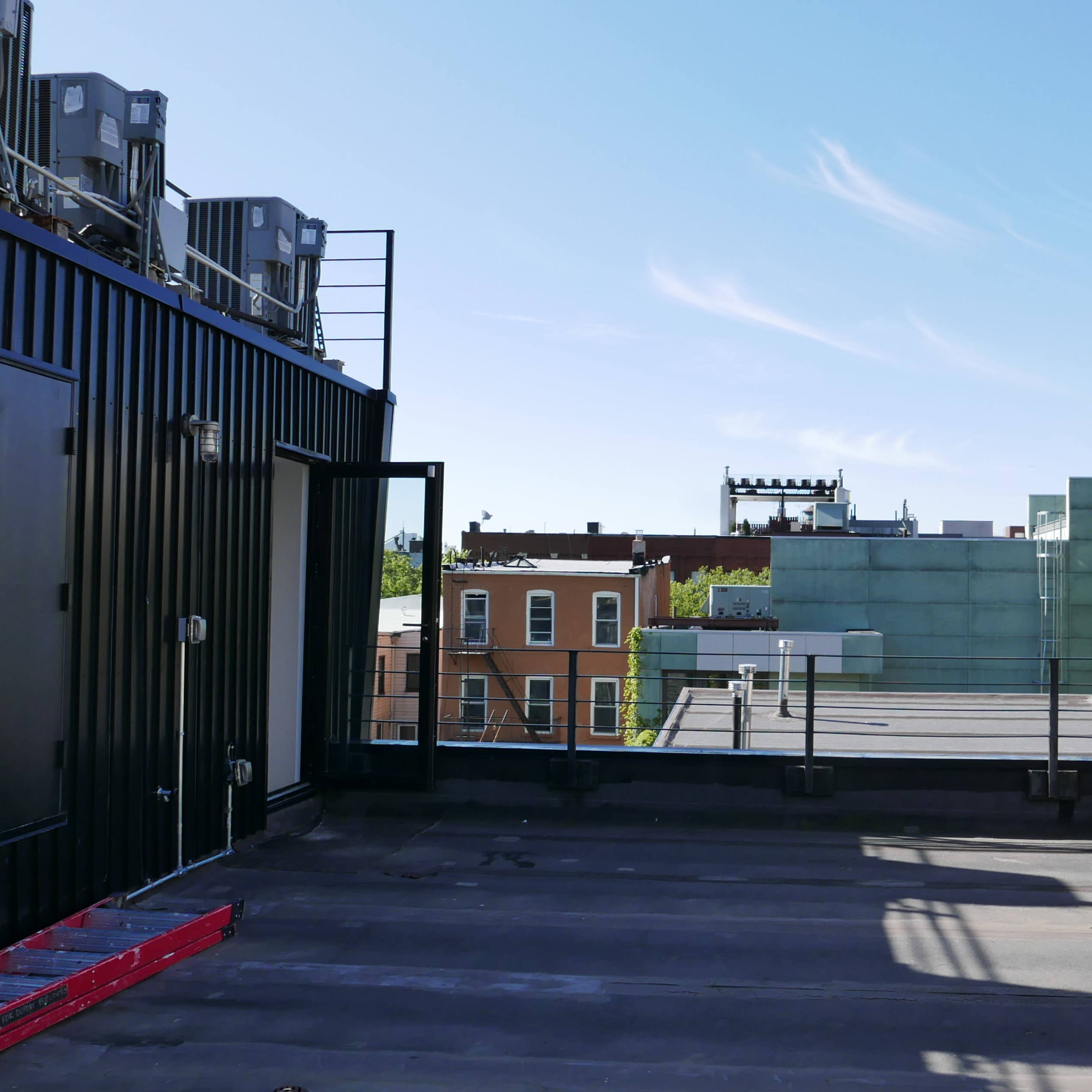 A flat rooftop with various cooling units, adjacent buildings, and a clear blue sky.