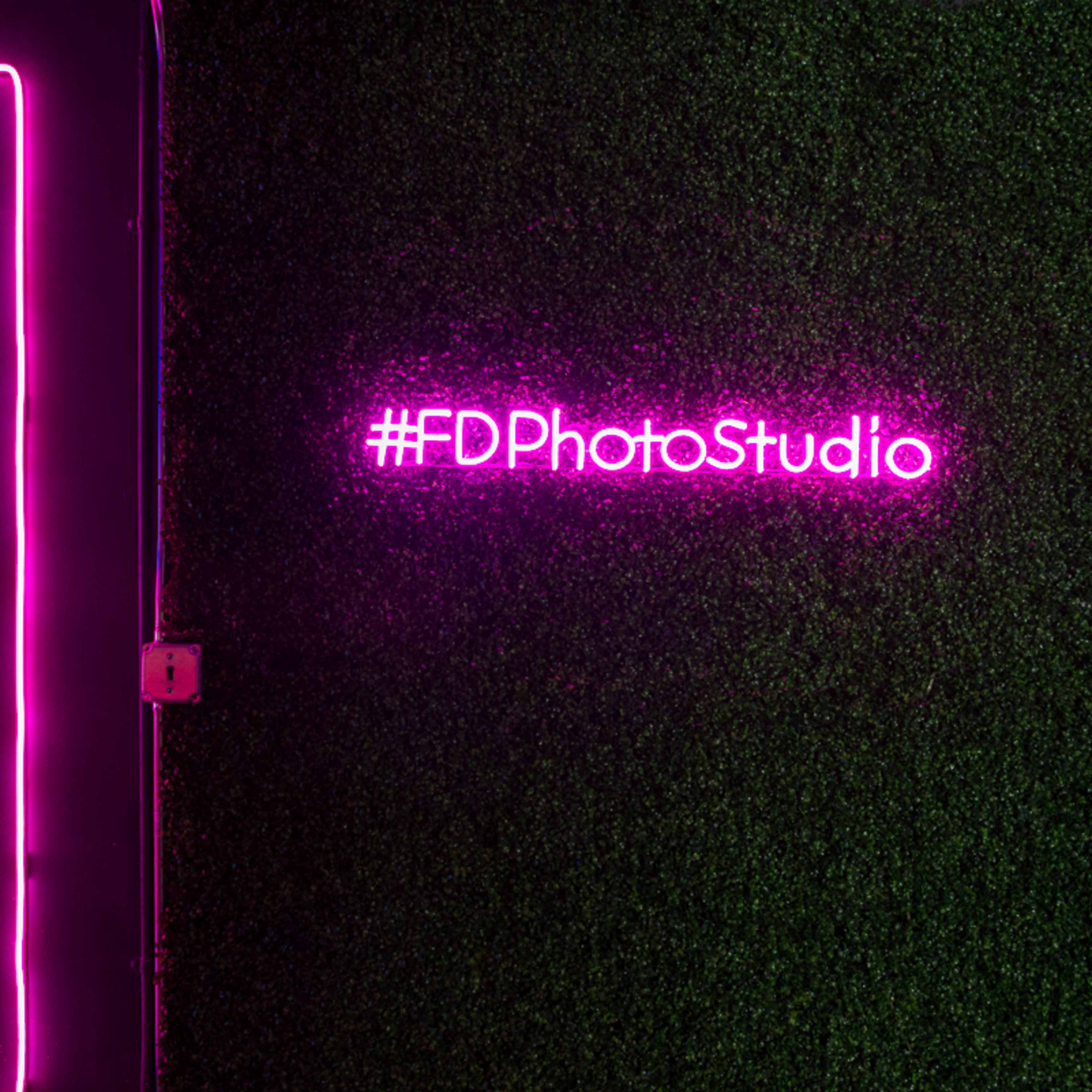 A green wall with neon light designs in pink, including the hashtag #FDPhotoStudio.