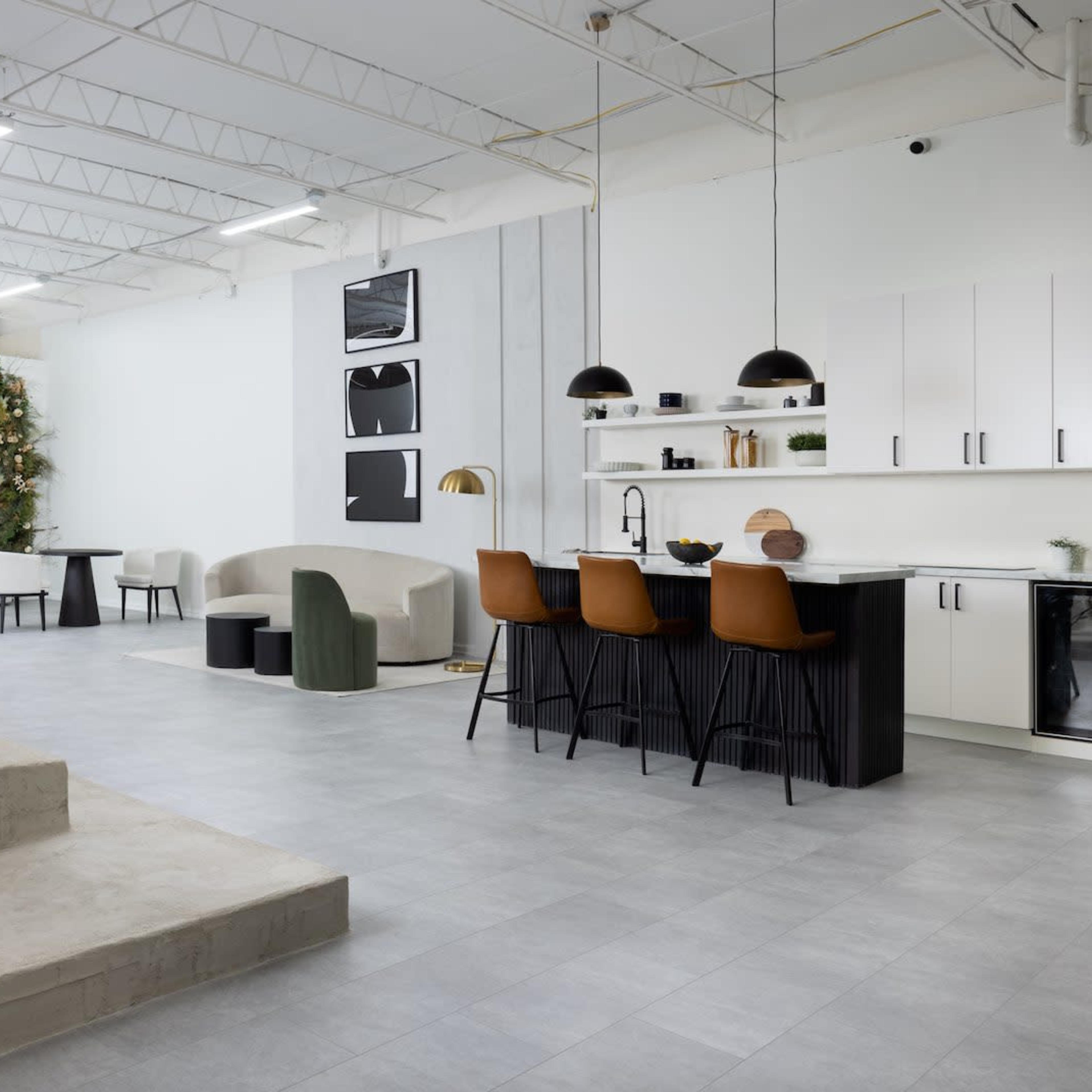 A modern open-concept living space featuring a kitchen with bar seating, a dining area, and minimalist furniture against a light-colored backdrop.