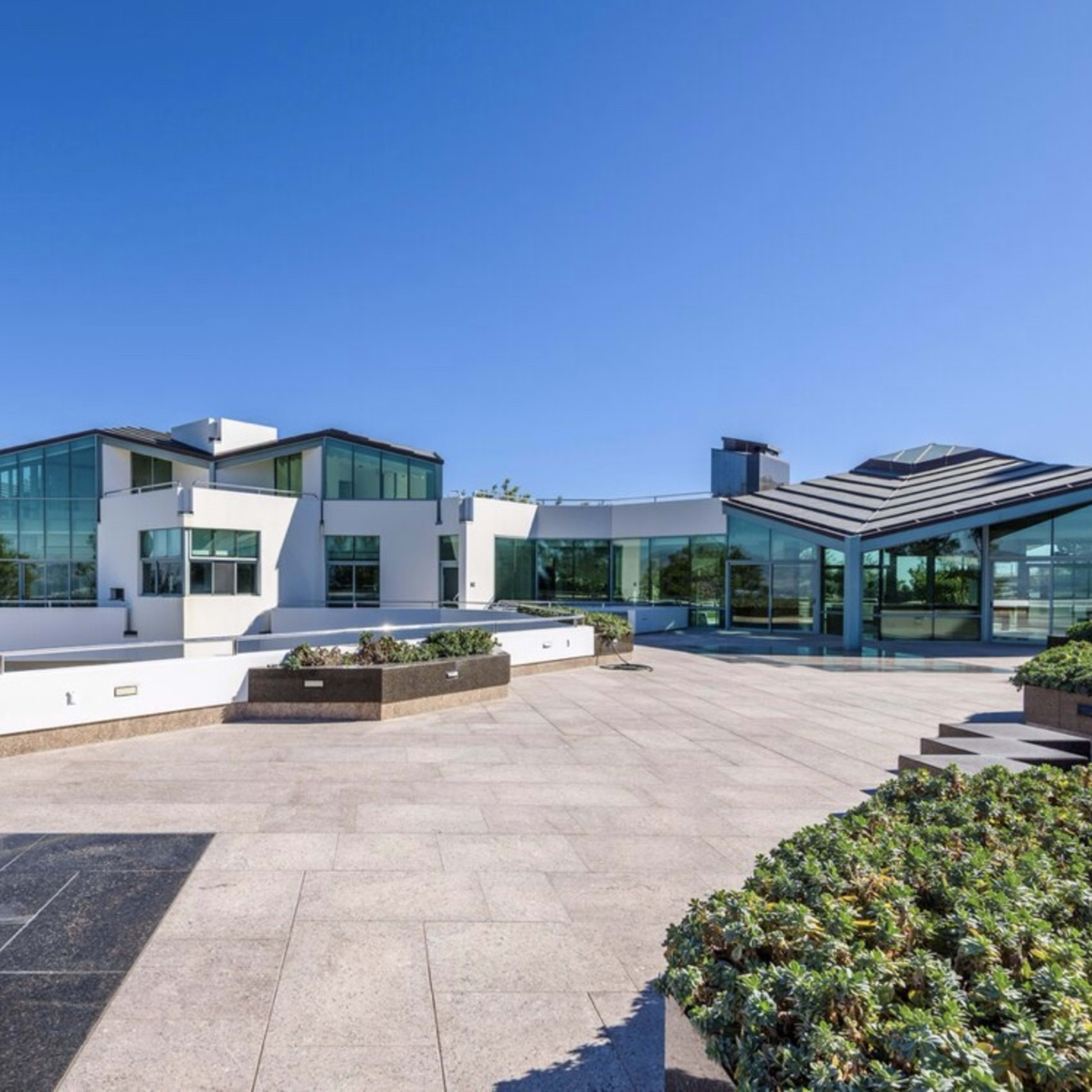 A modern, multi-level house with extensive glass walls and a stone patio garden.