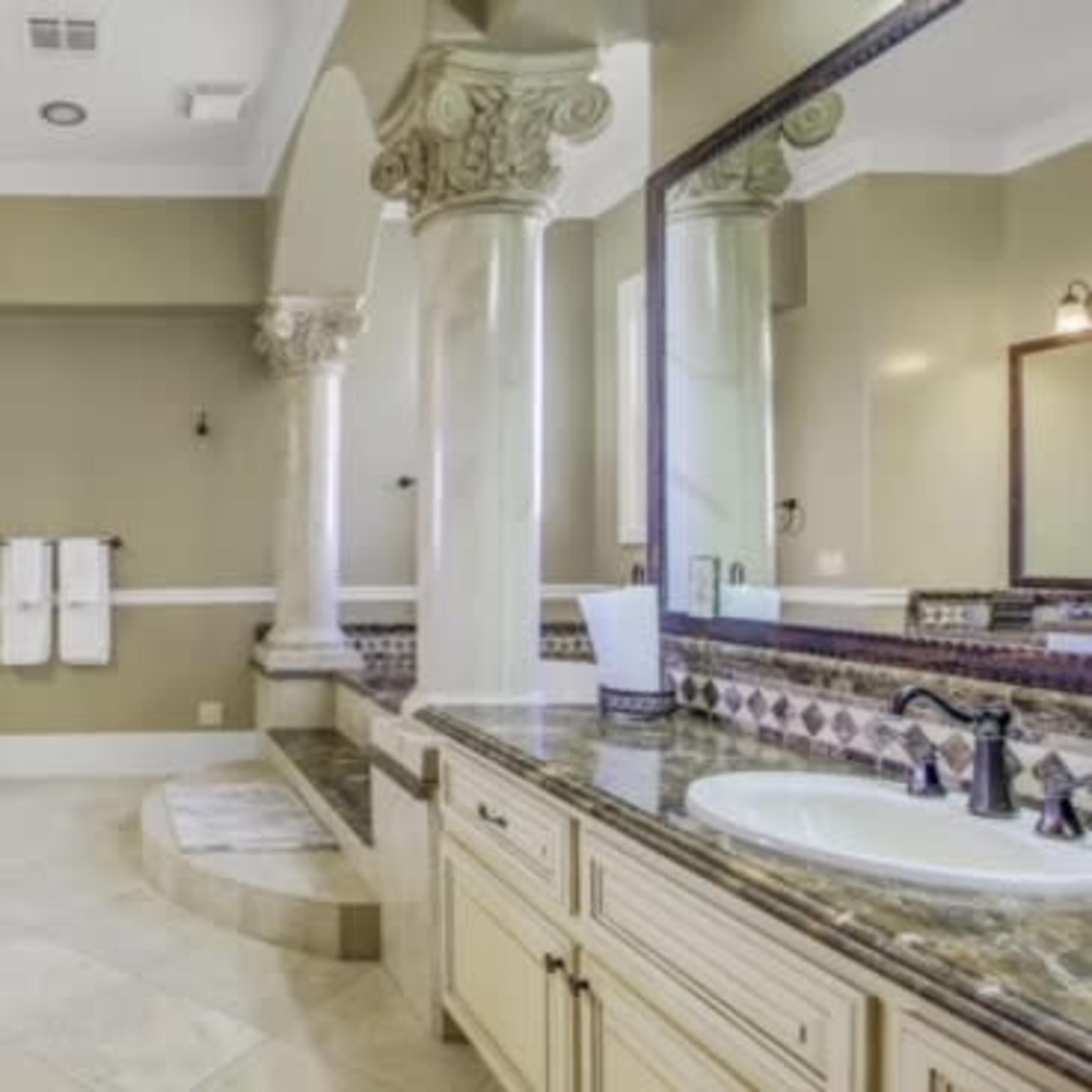 A spacious bathroom with dual sinks, large mirrors, and elegant columns.