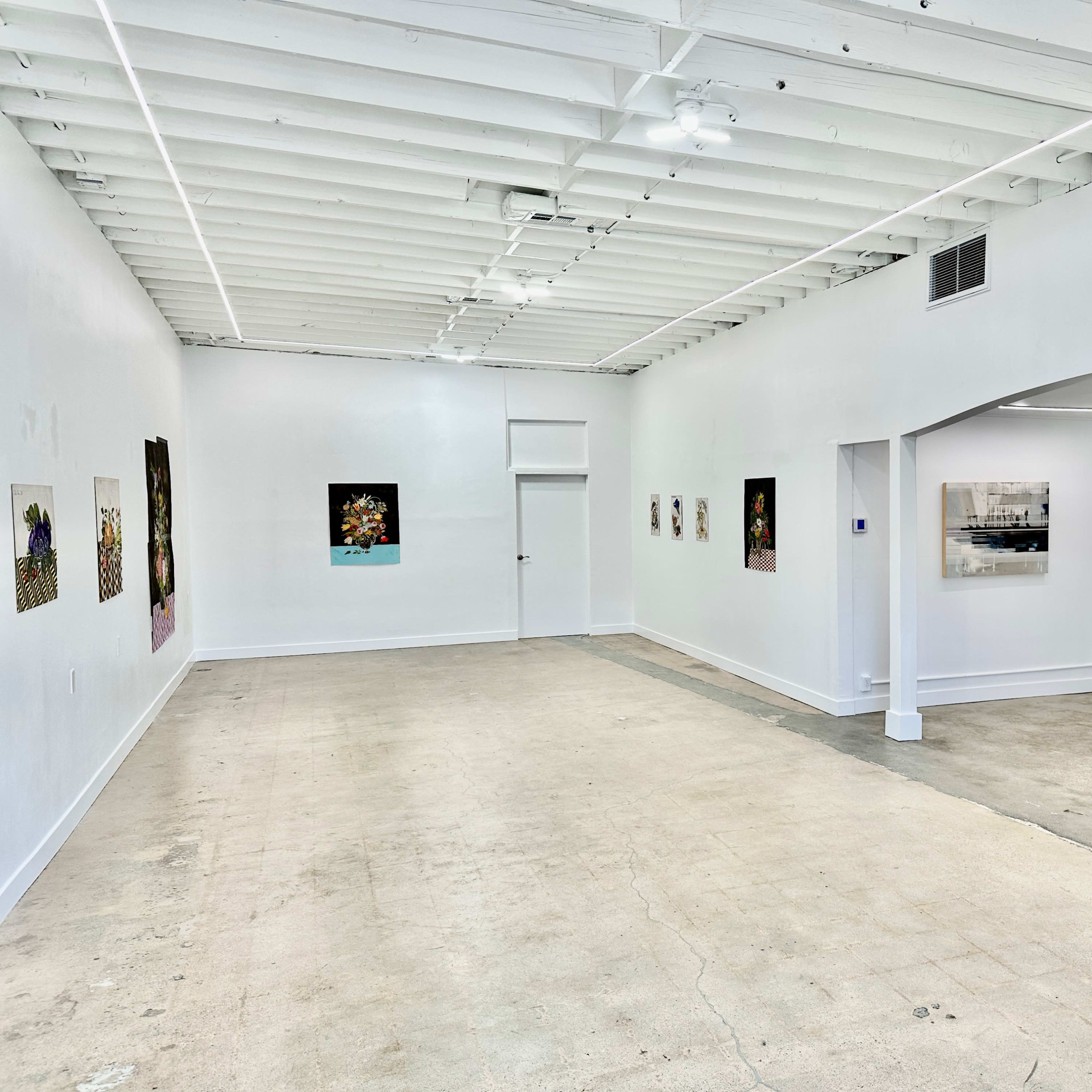 A spacious art gallery with white walls, showcasing various artworks hung on the walls and a concrete floor.