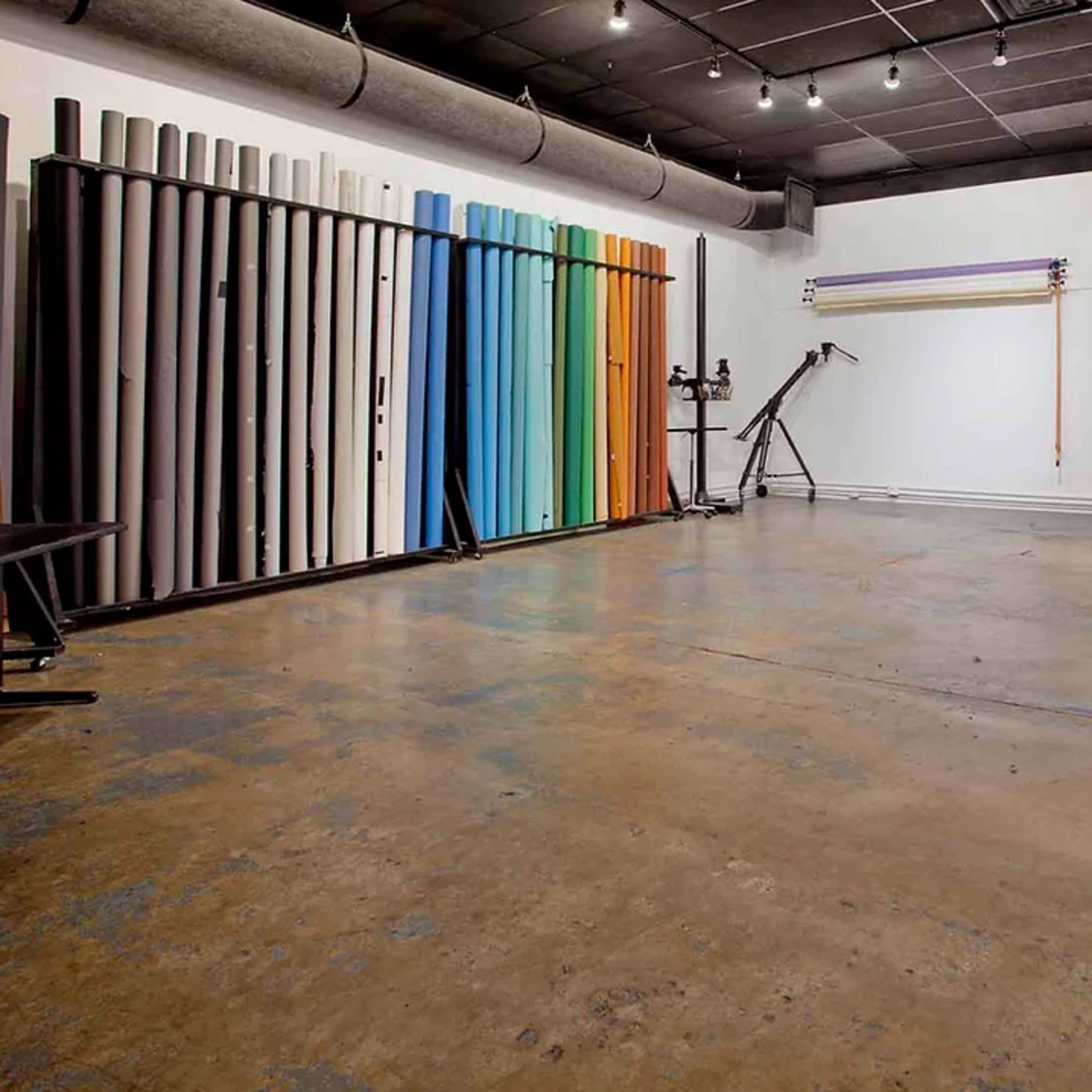 An empty studio space with a concrete floor and several rolls of backdrop paper in various colors against the walls.
