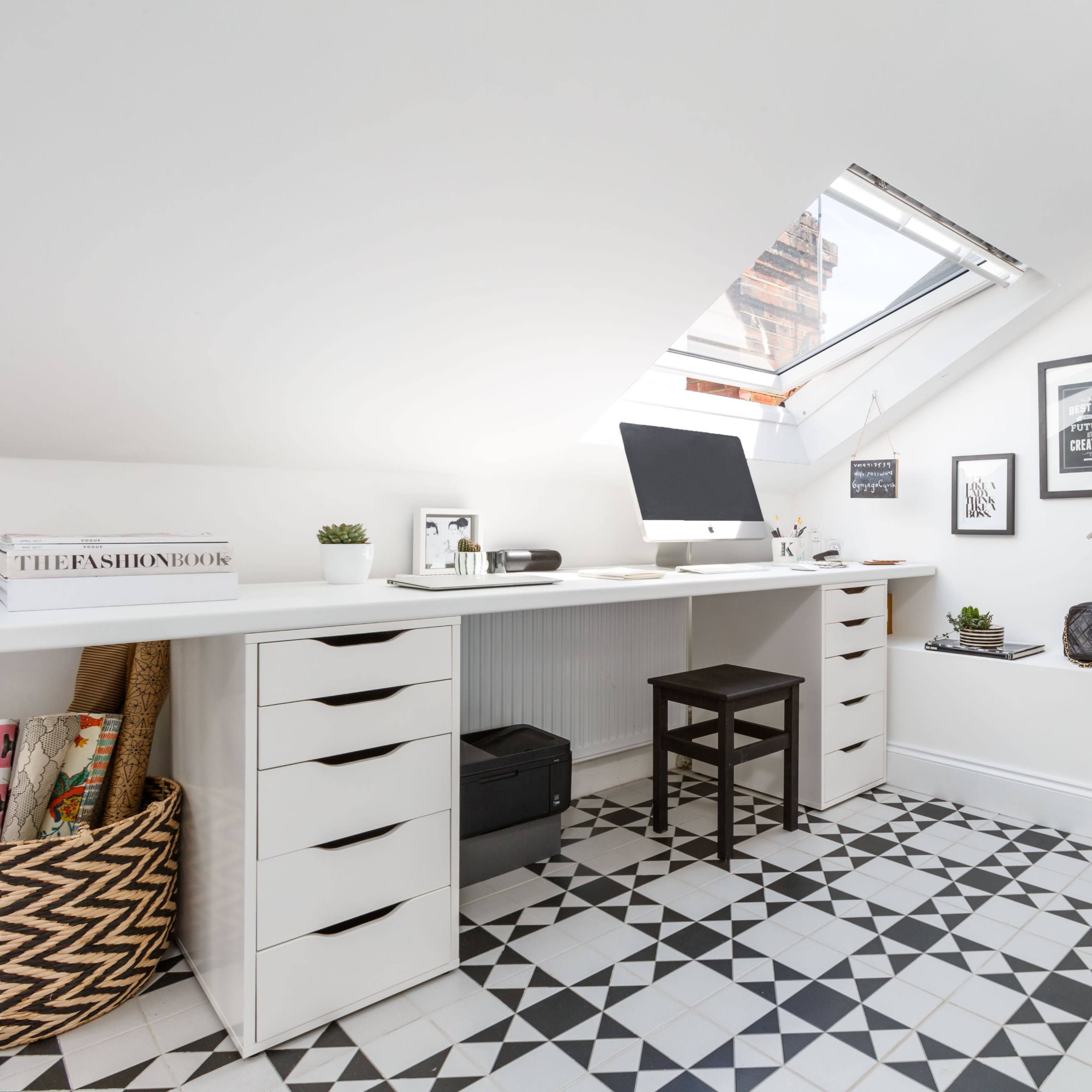 A modern attic office space with a desk and computer under a slanted ceiling, featuring patterned tile flooring and a small bathroom area visible through an open door.