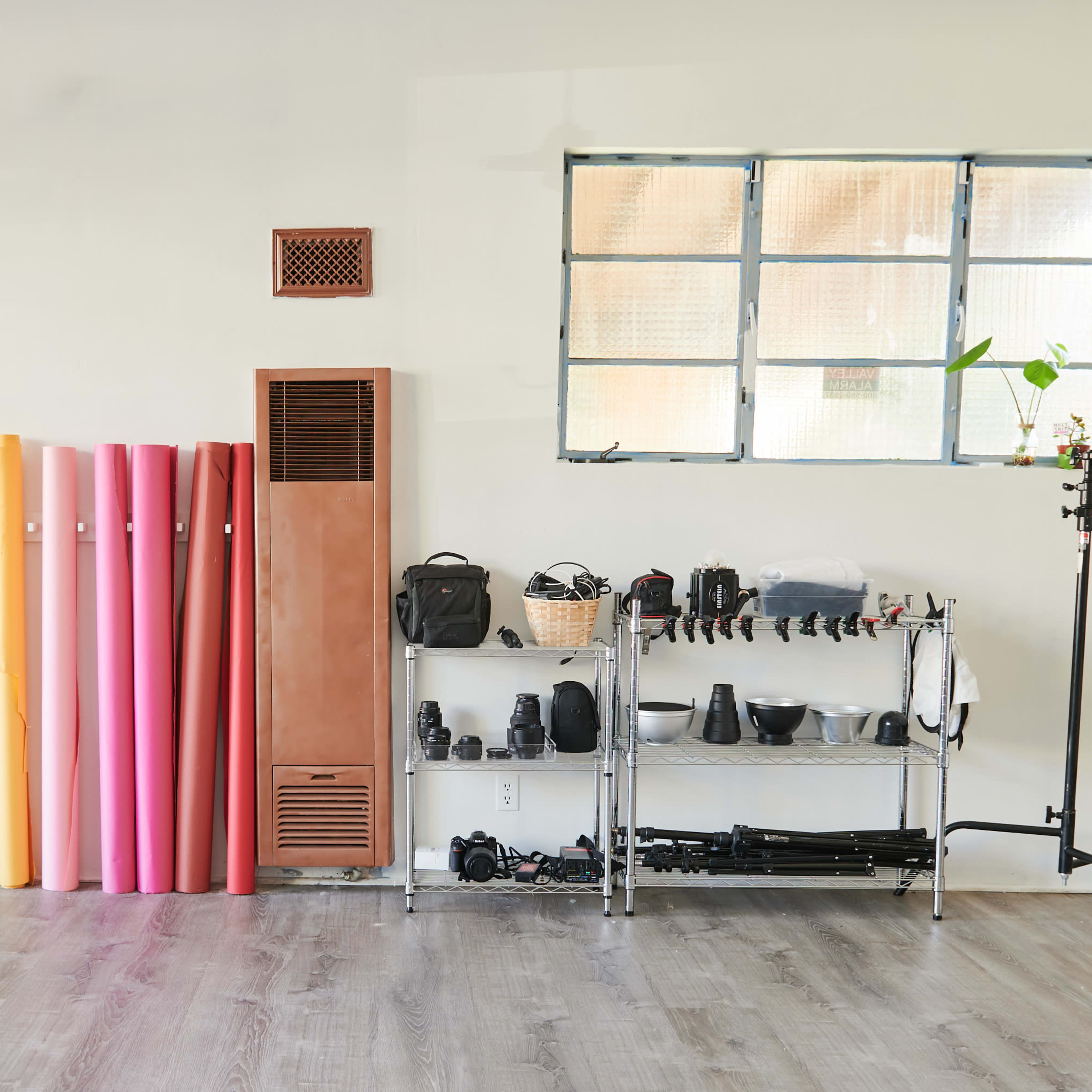 A studio space with a row of colored backdrop rolls along one wall, a wooden shelf holding photography equipment, and a director's chair next to a tripod.