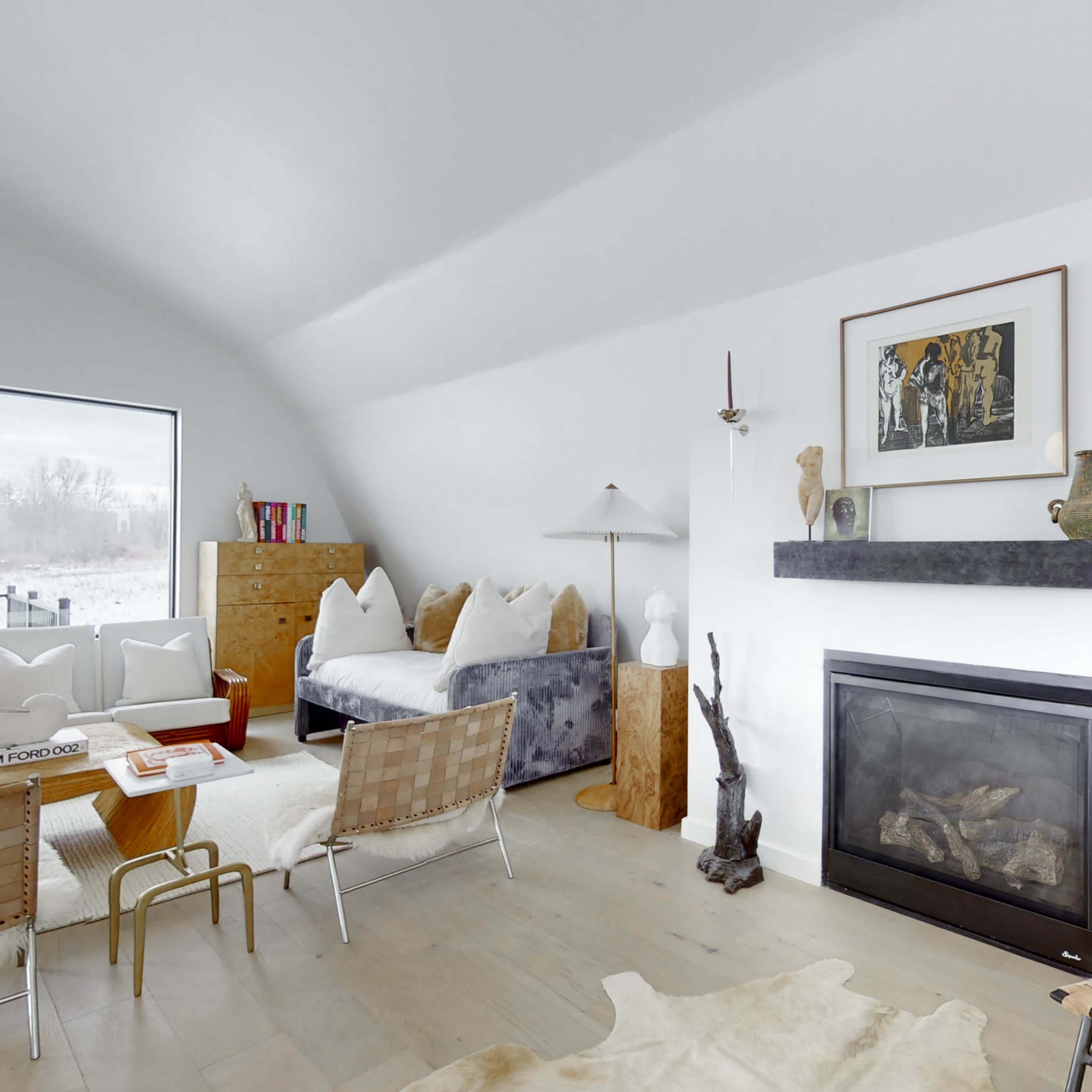 A modern living room with a minimalist design featuring a fireplace, art on the walls, and various seating arrangements.