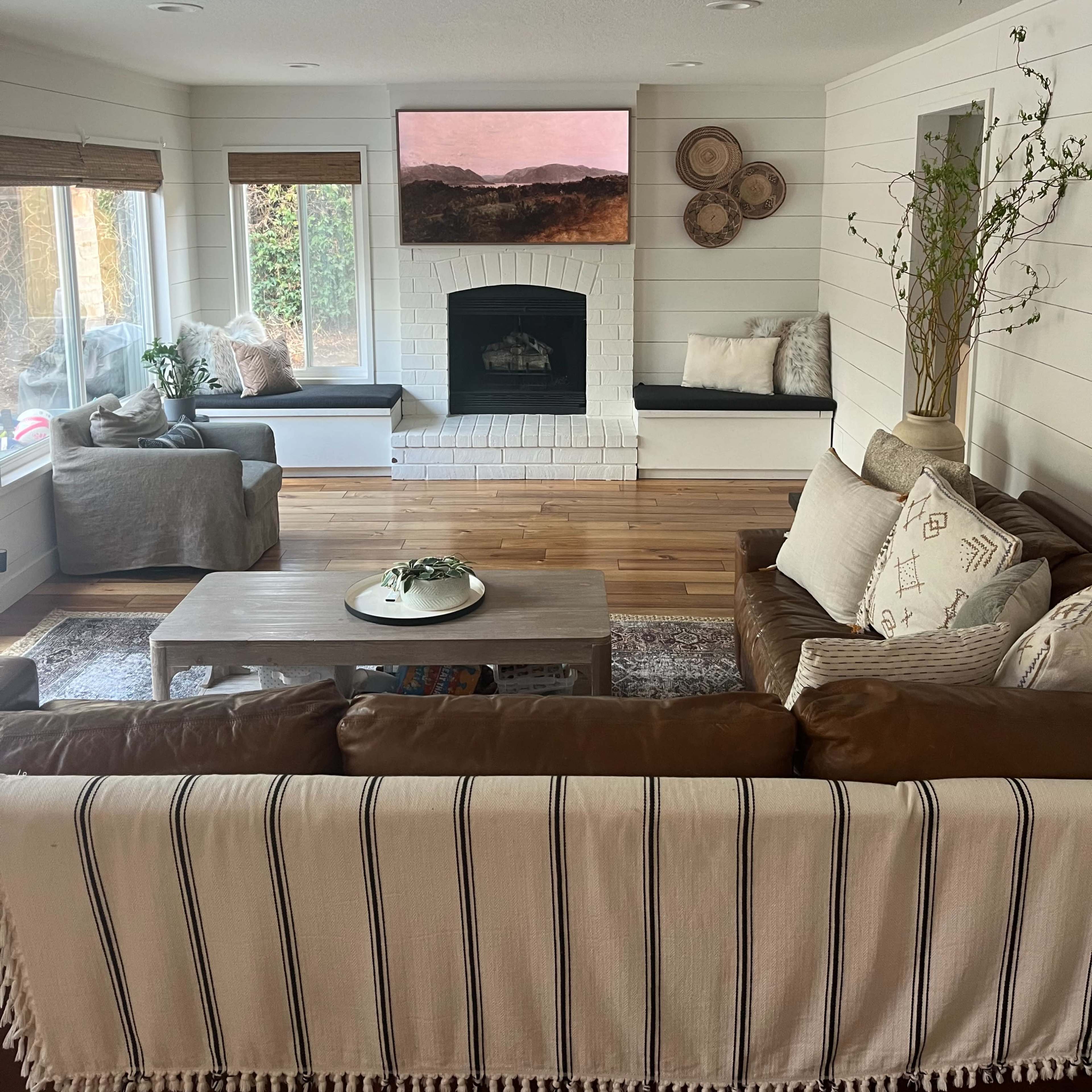 A well-lit living room features a fireplace, two benches, a coffee table, and a large wall-mounted artwork.