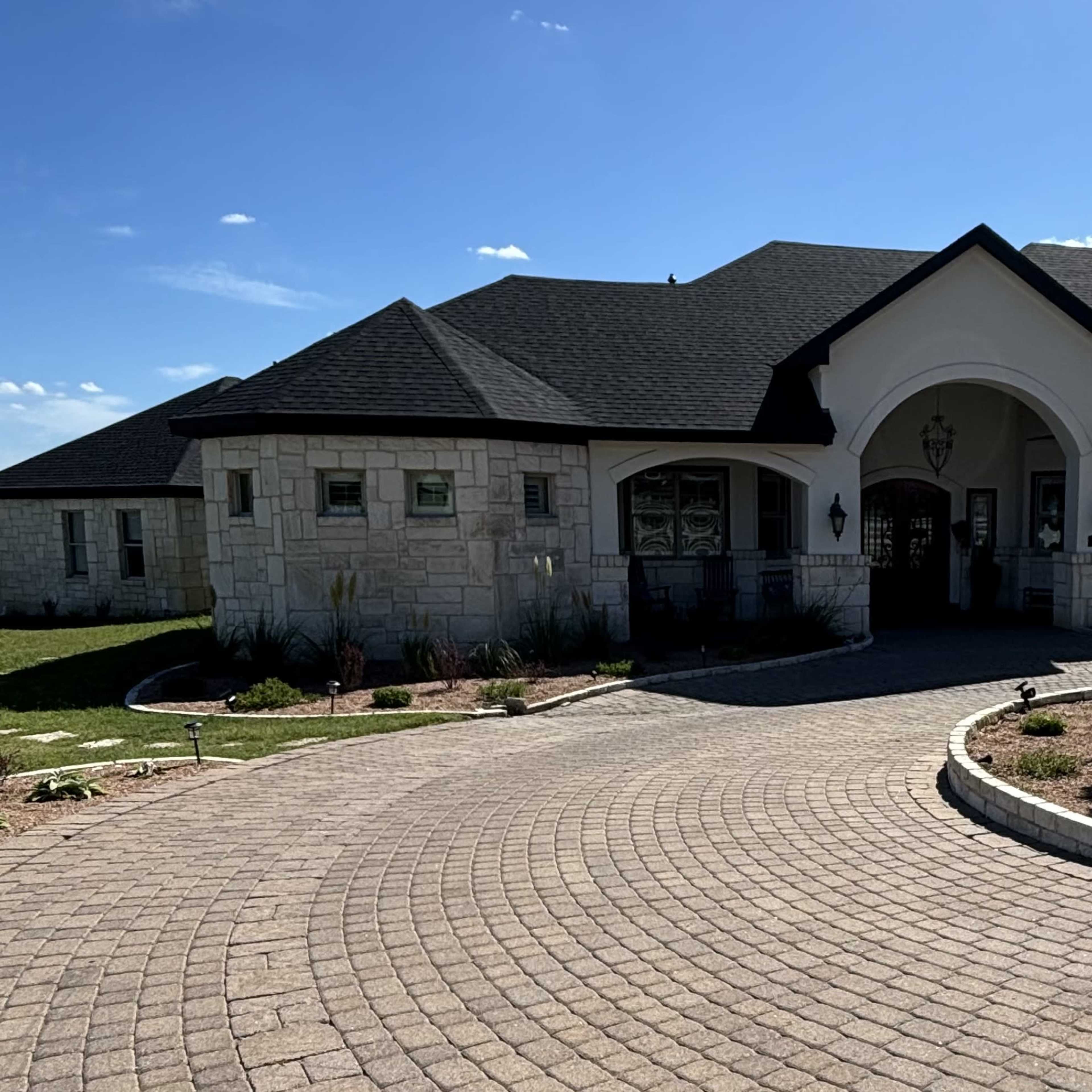 A sprawling single-story house with a curved entrance, surrounded by a paved driveway and landscaped areas.