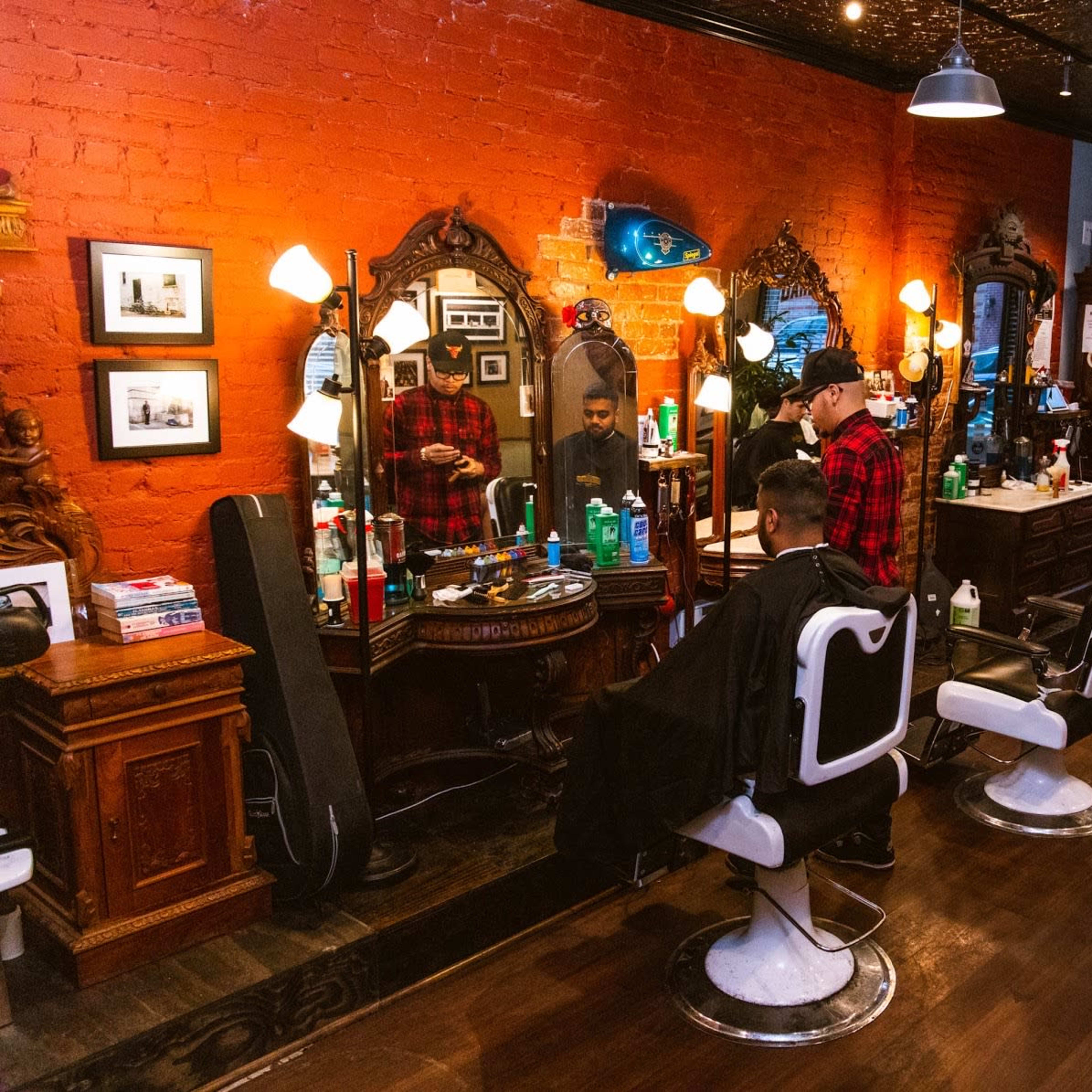 A barbershop interior features several vintage barber chairs, mirrors, and shelves filled with grooming products against a brick wall.