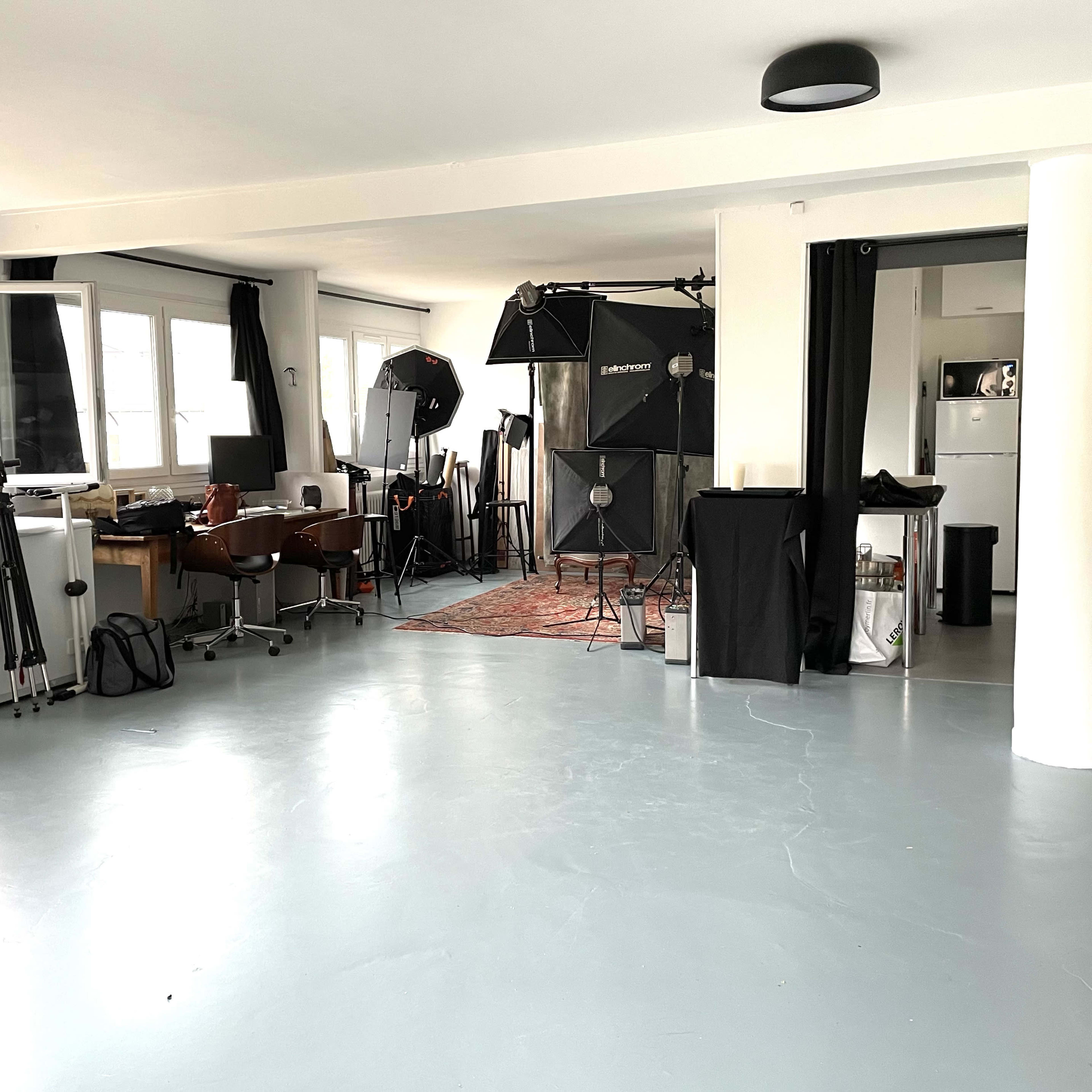 A spacious studio with photography equipment, including tripods and backdrops, and furniture for a work setup.