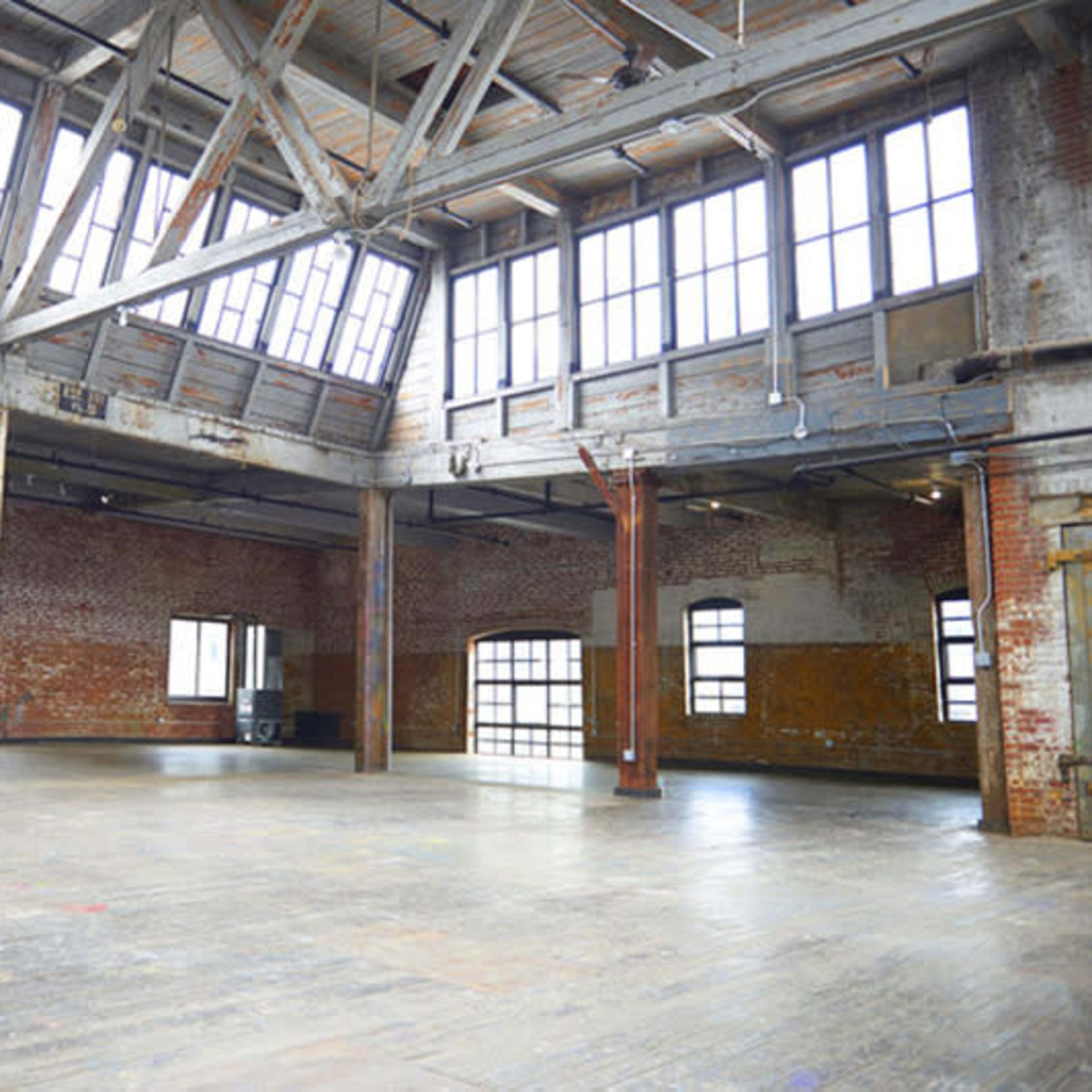 A large, open space with exposed brick walls, wooden beams, and large windows allowing natural light to flood the interior.