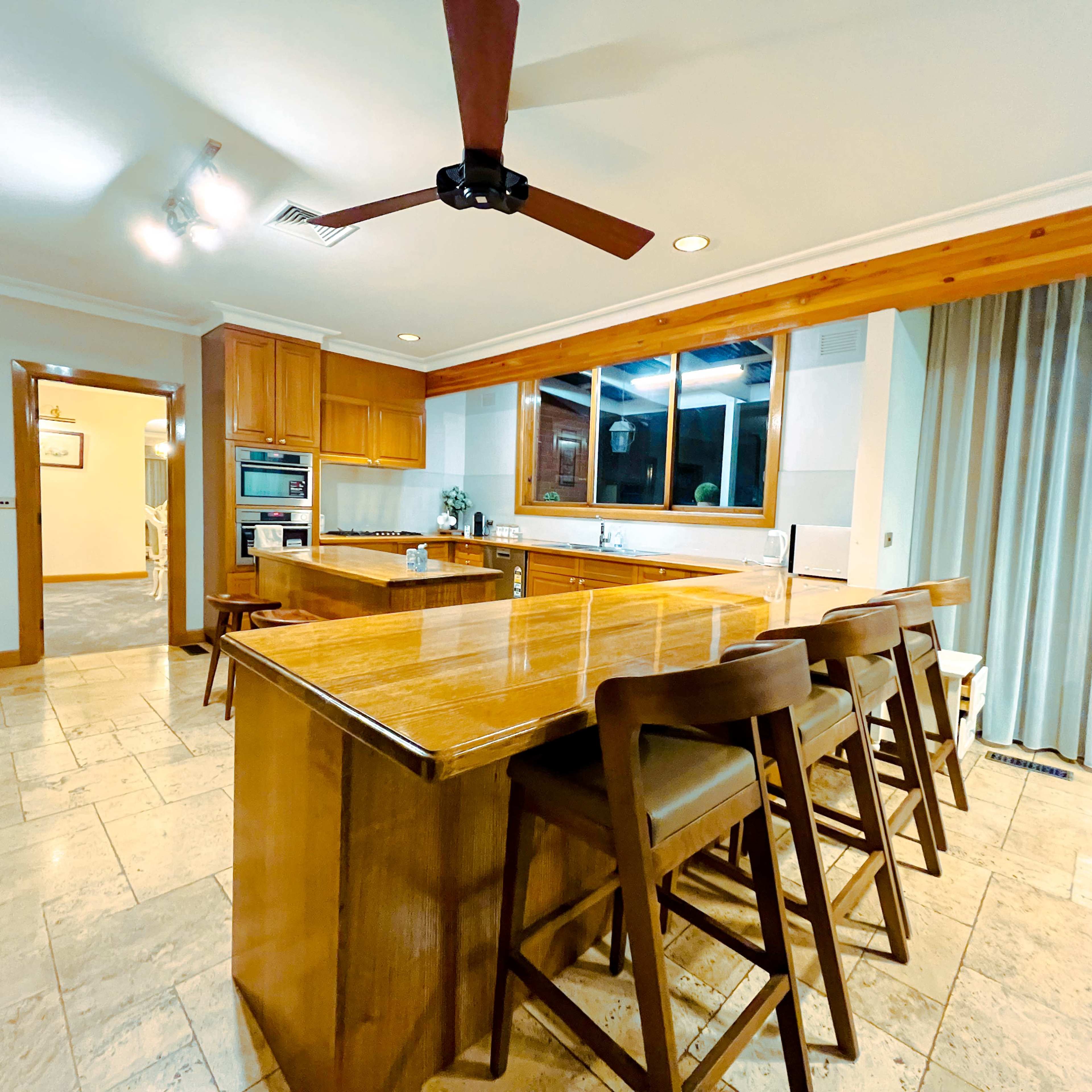 A spacious kitchen featuring a wooden island with seating, modern appliances, and large windows allowing natural light to enter.