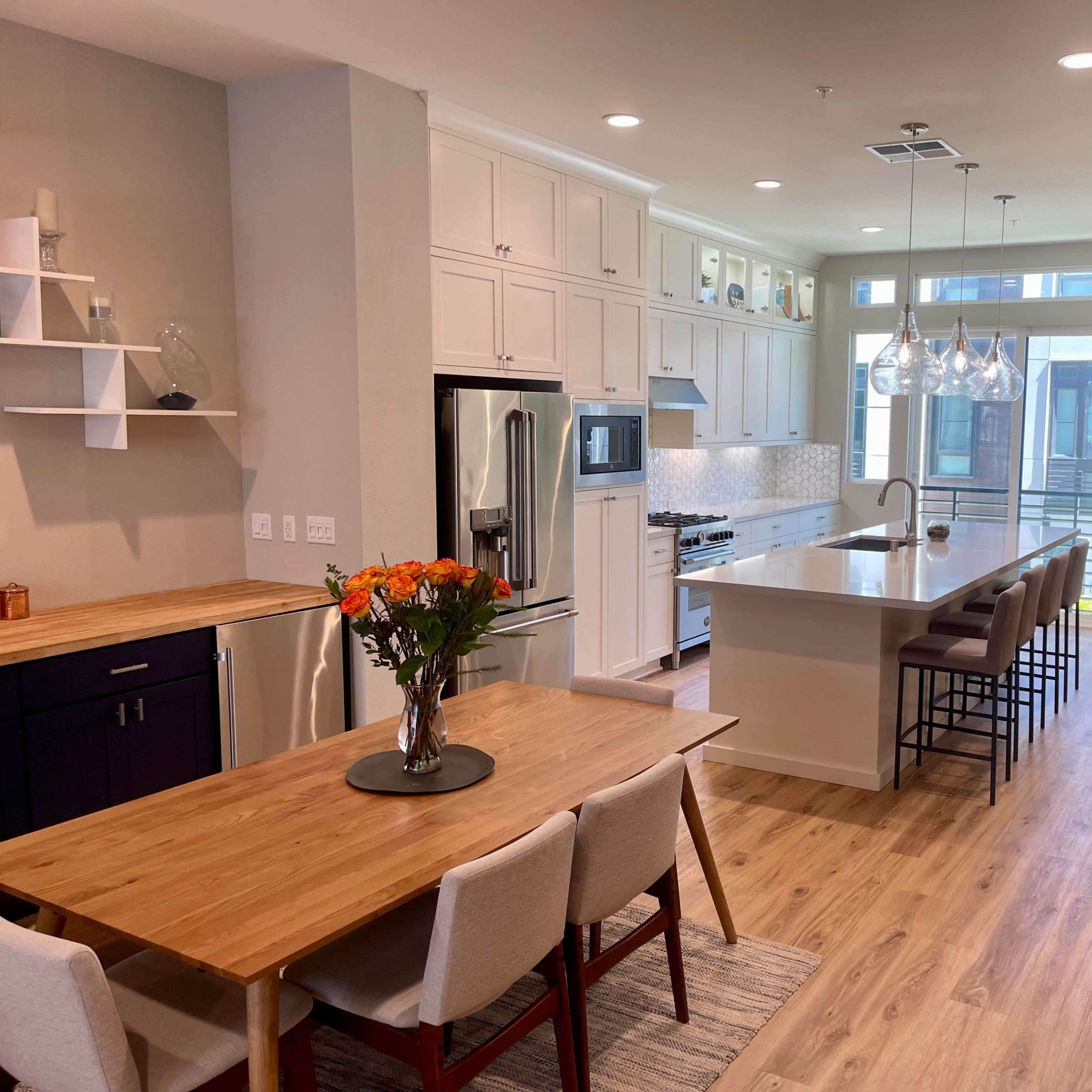 A modern kitchen and dining area with a long island, dining table, and large windows letting in natural light.