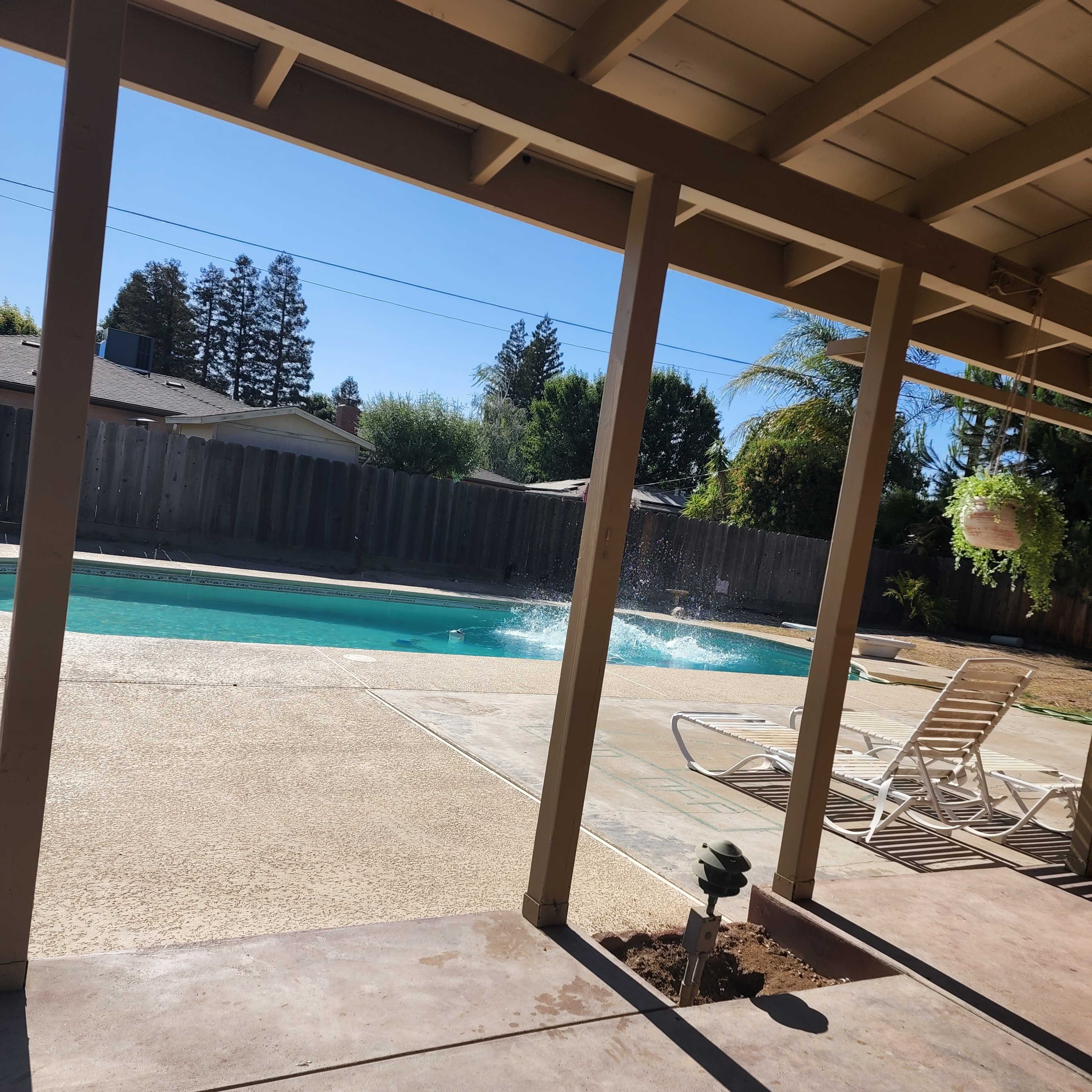 A clear swimming pool with splashes of water and a patio area with lounge chairs under a covered porch.