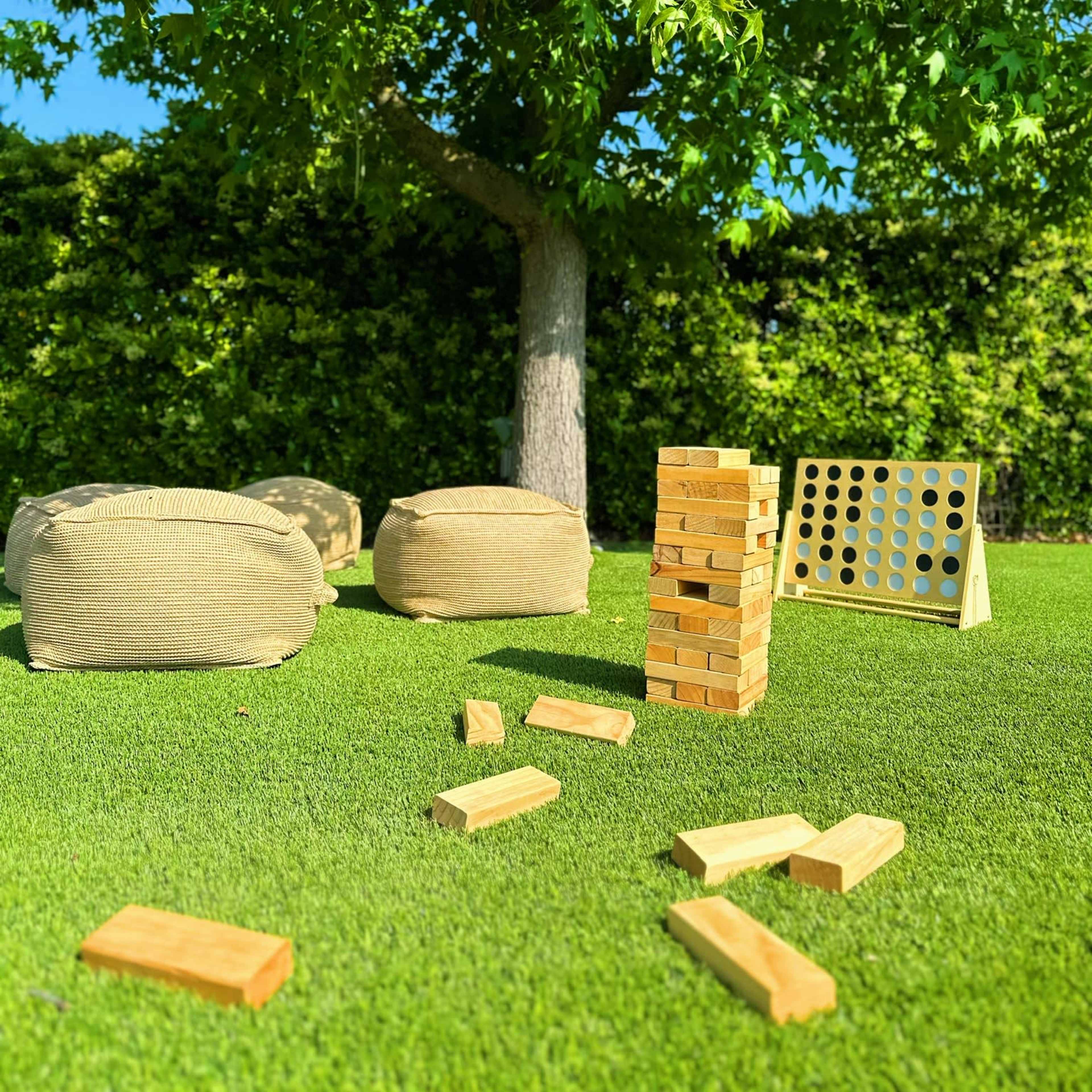 A game setup featuring a Jenga tower, Connect Four grid, and scattered wooden blocks on a green lawn under a tree.
