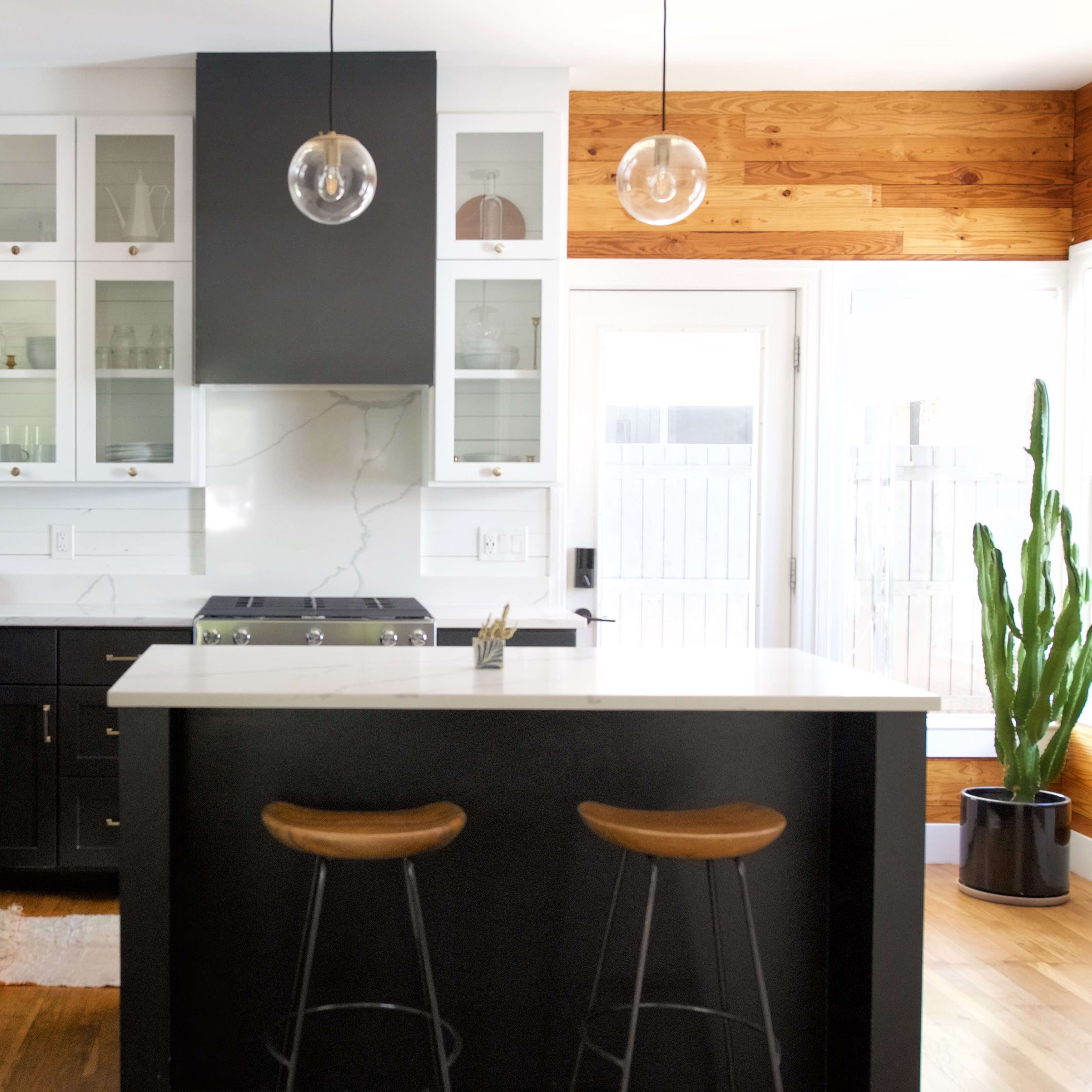 A modern kitchen features dark cabinetry, a central island with two stools, and large windows allowing natural light.