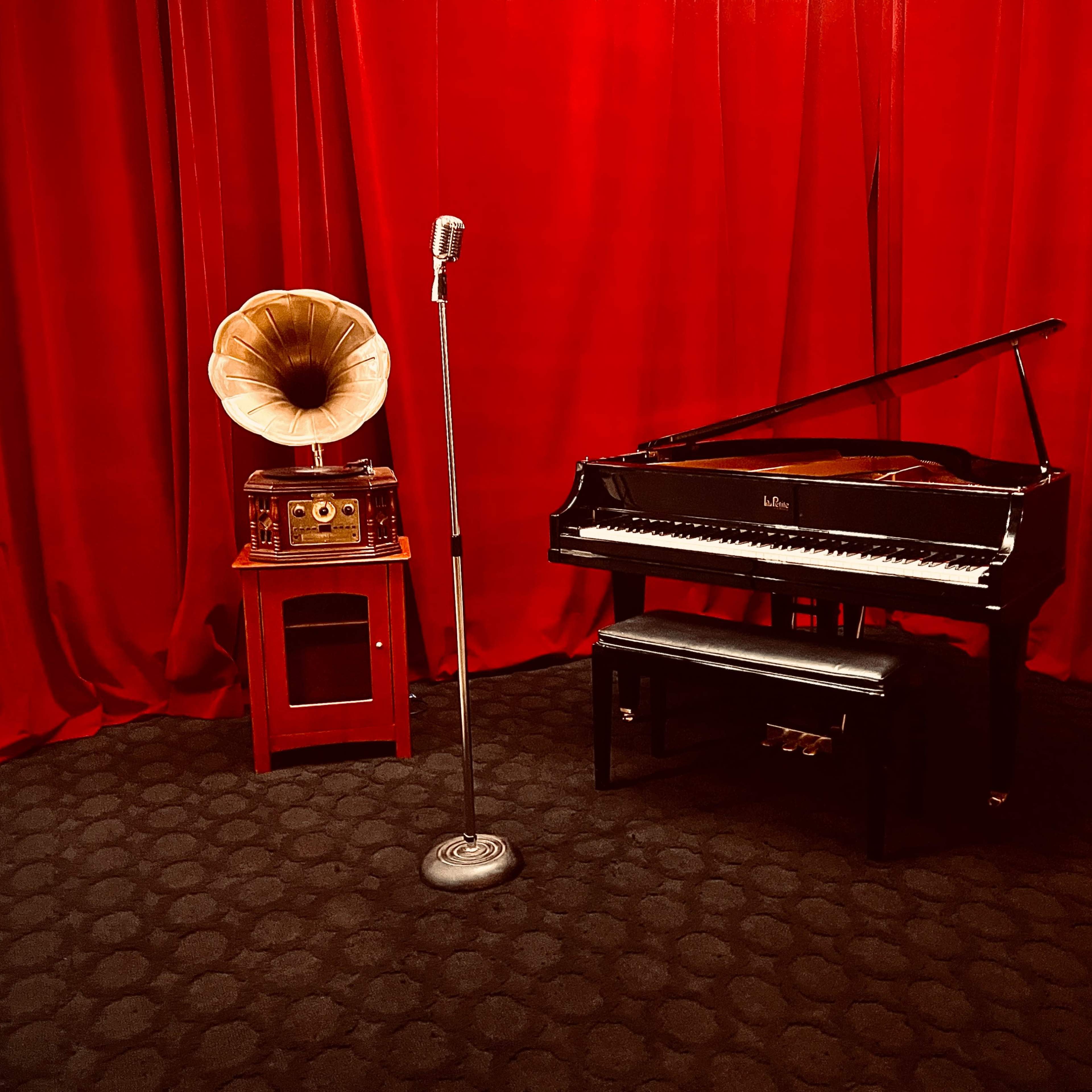 A grand piano and a vintage gramophone are set against a red velvet backdrop, with a microphone on a stand nearby.